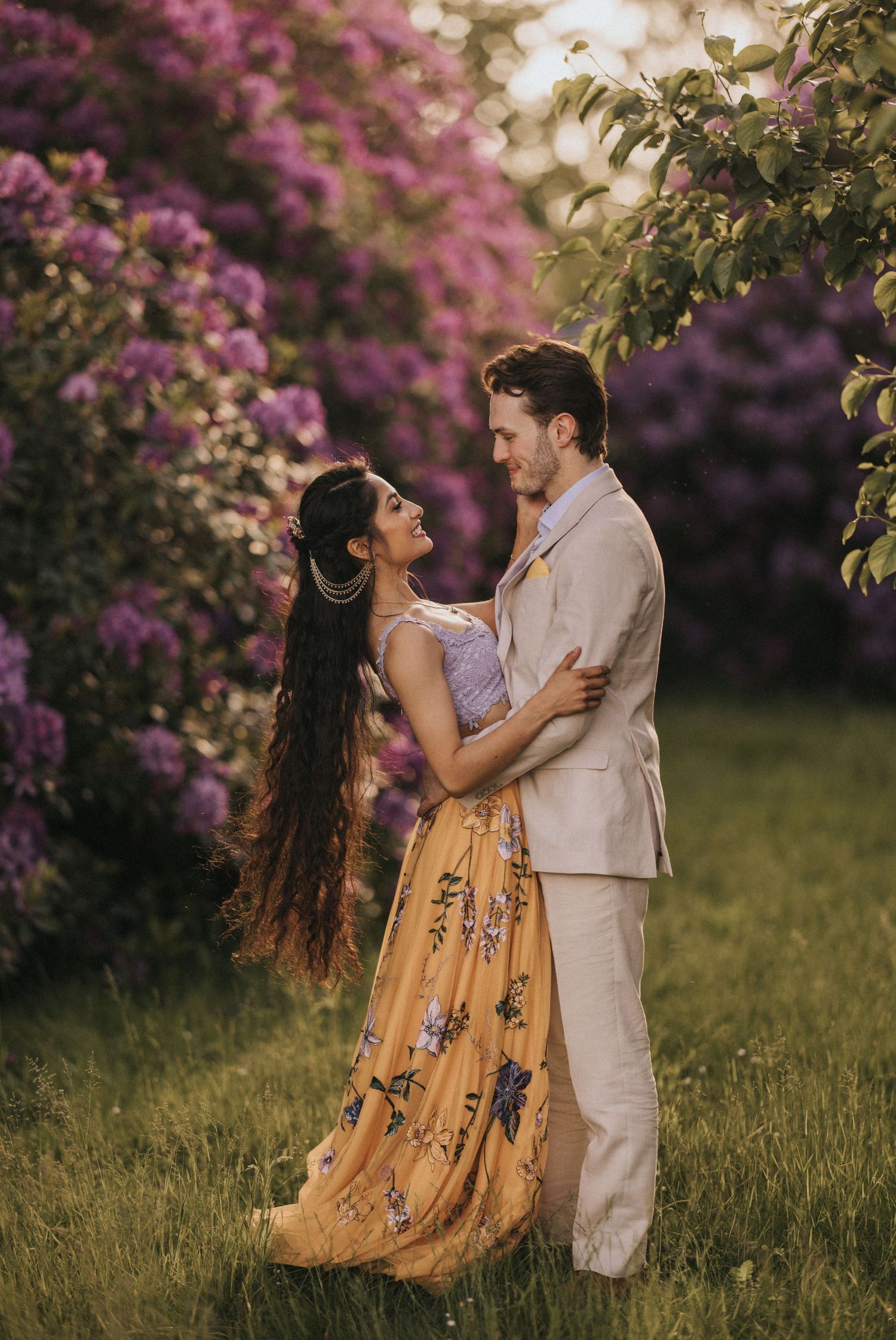 Romantic couple embraces among blooming pink flowers in garden during spring photoshoot.