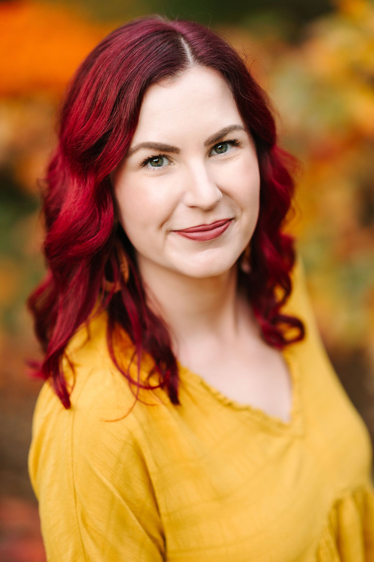 Portrait of a woman in yellow sweater with red hair against colorful fall foliage.