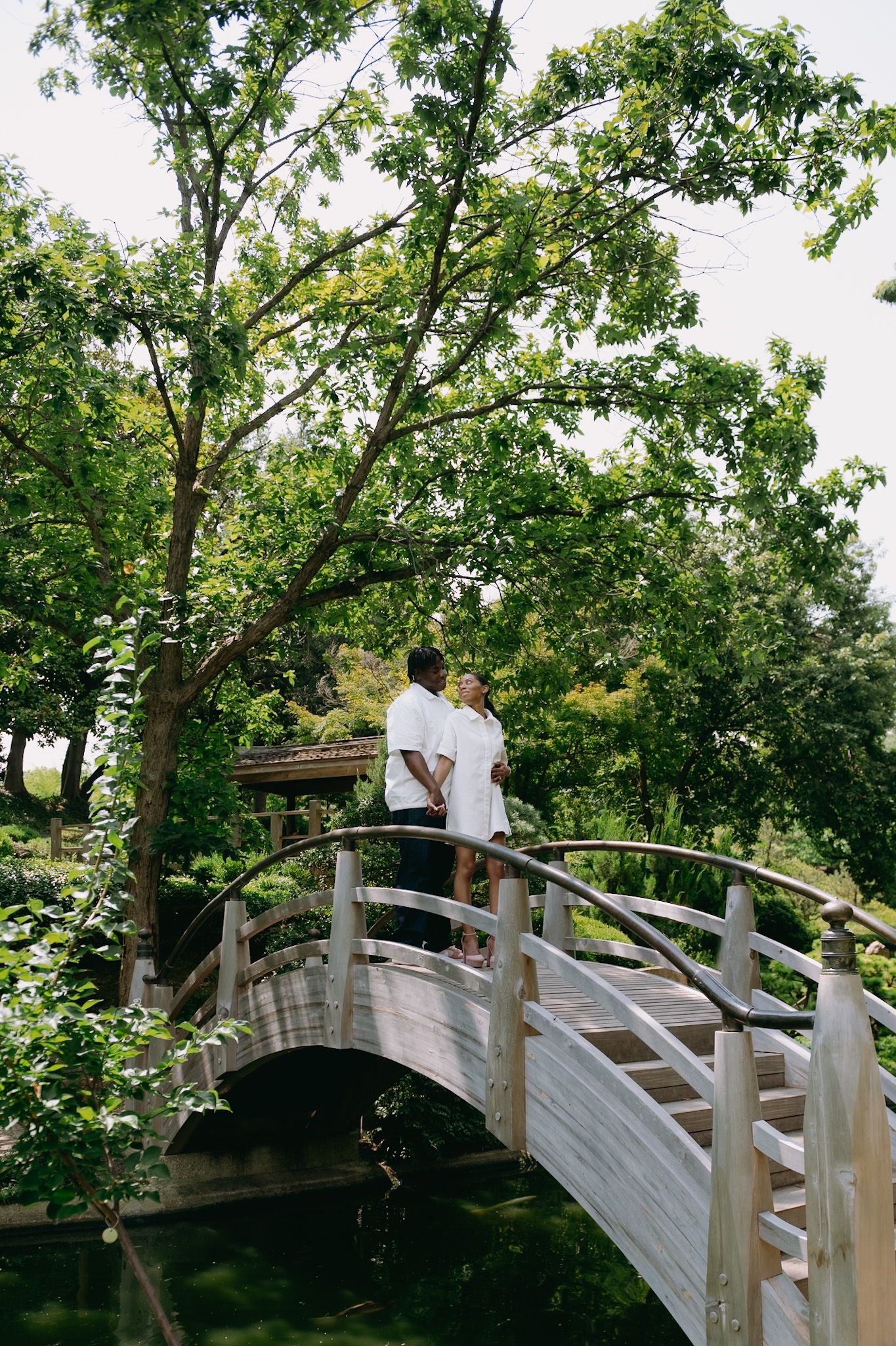 A scenic arched white bridge curves through lush green trees in a garden setting.