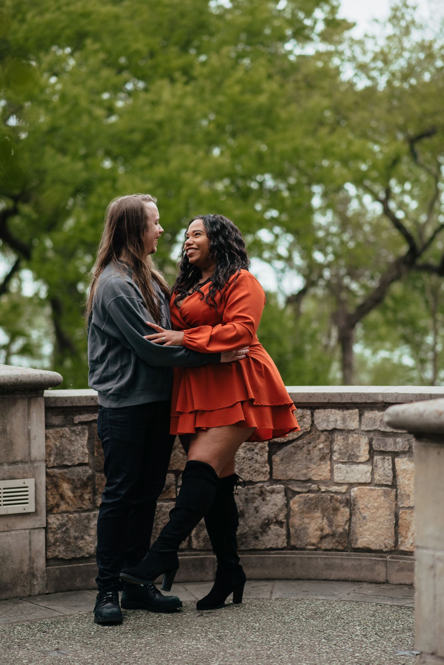 Two people share affectionate moments against a stone wall backdrop.