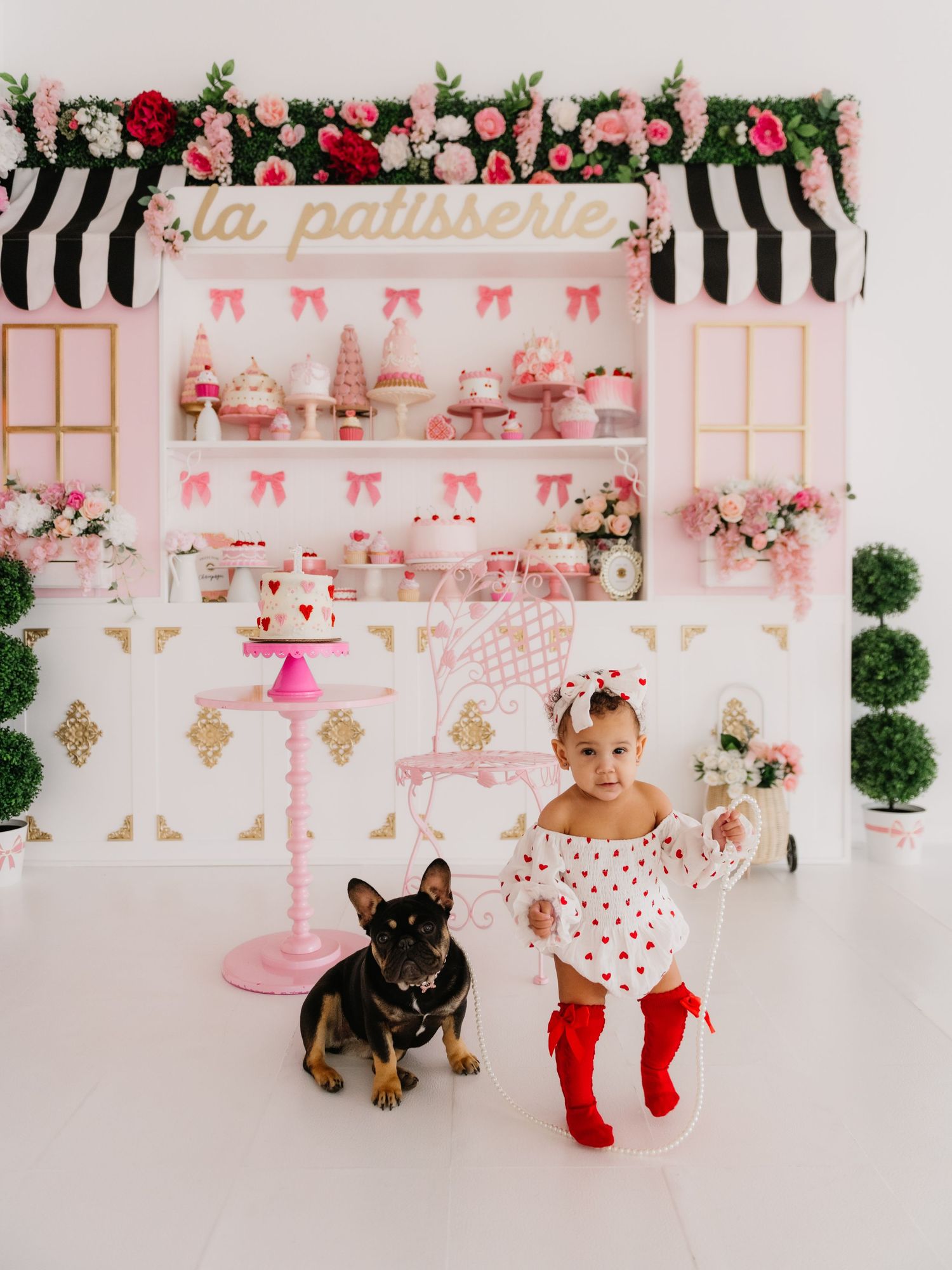 Pink and white themed party setup with floral decorations and a small dog in formal attire.