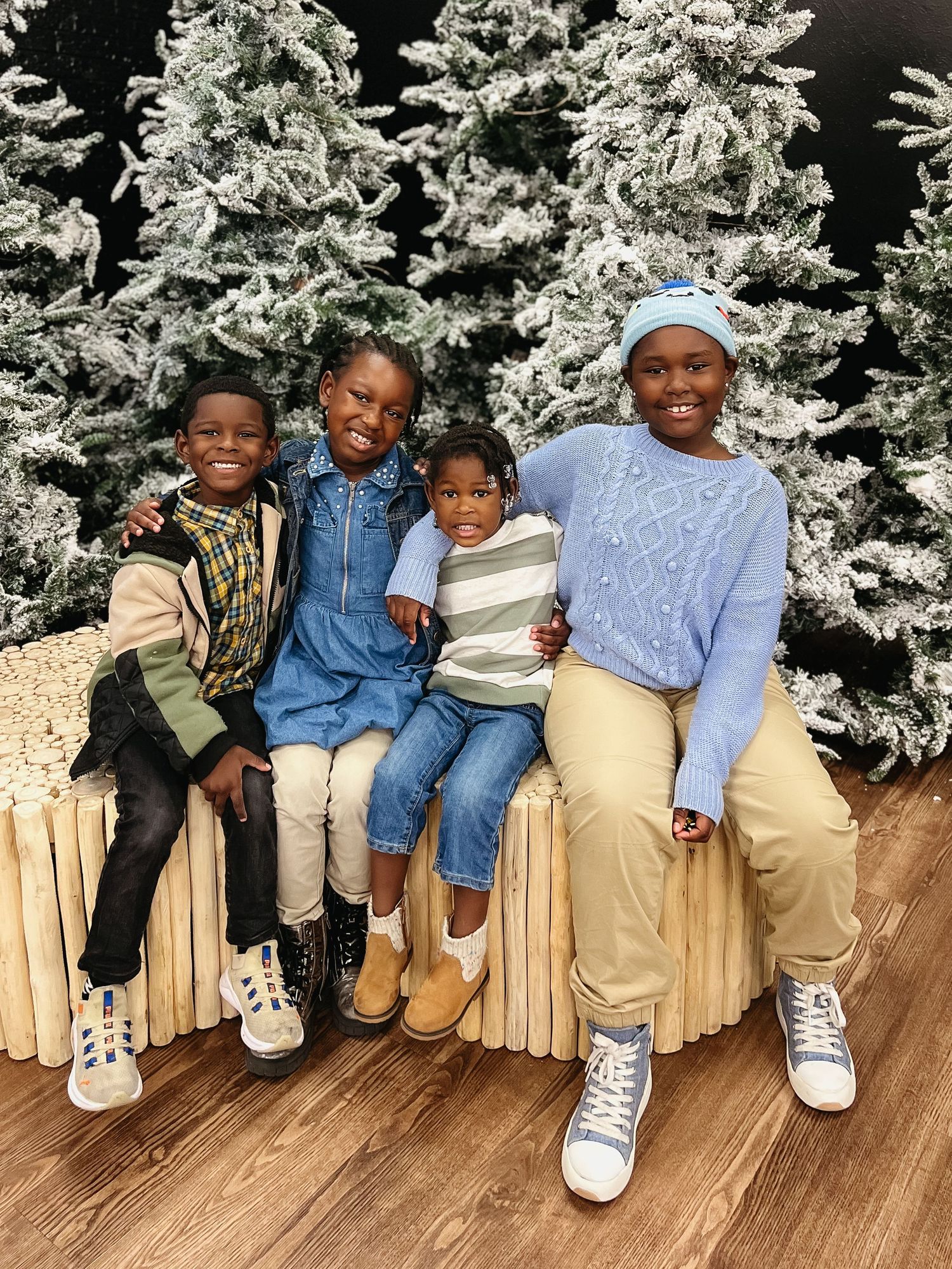 Row of winter boots and jeans against snowy white Christmas trees on wooden flooring.