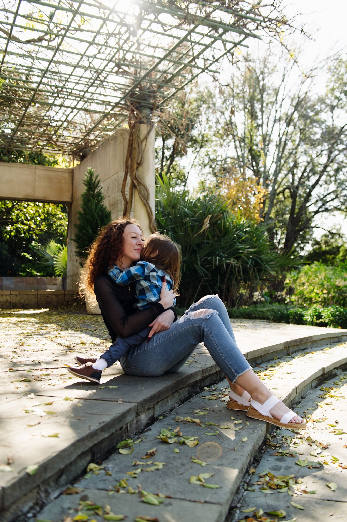 Person relaxing on stone steps under a pergola with dappled sunlight.