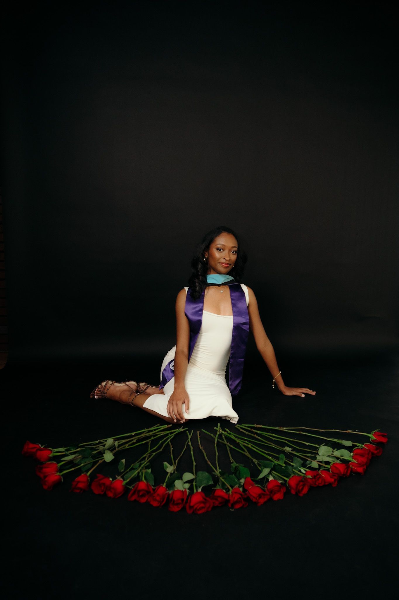 Figure in white dress lying on floor surrounded by long-stemmed red roses in dramatic lighting.