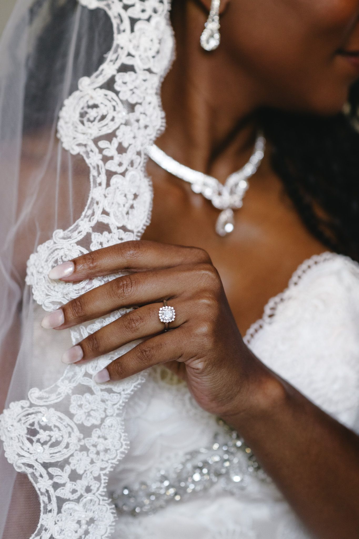 Close-up details of delicate lace wedding veil and sparkling diamond engagement ring.