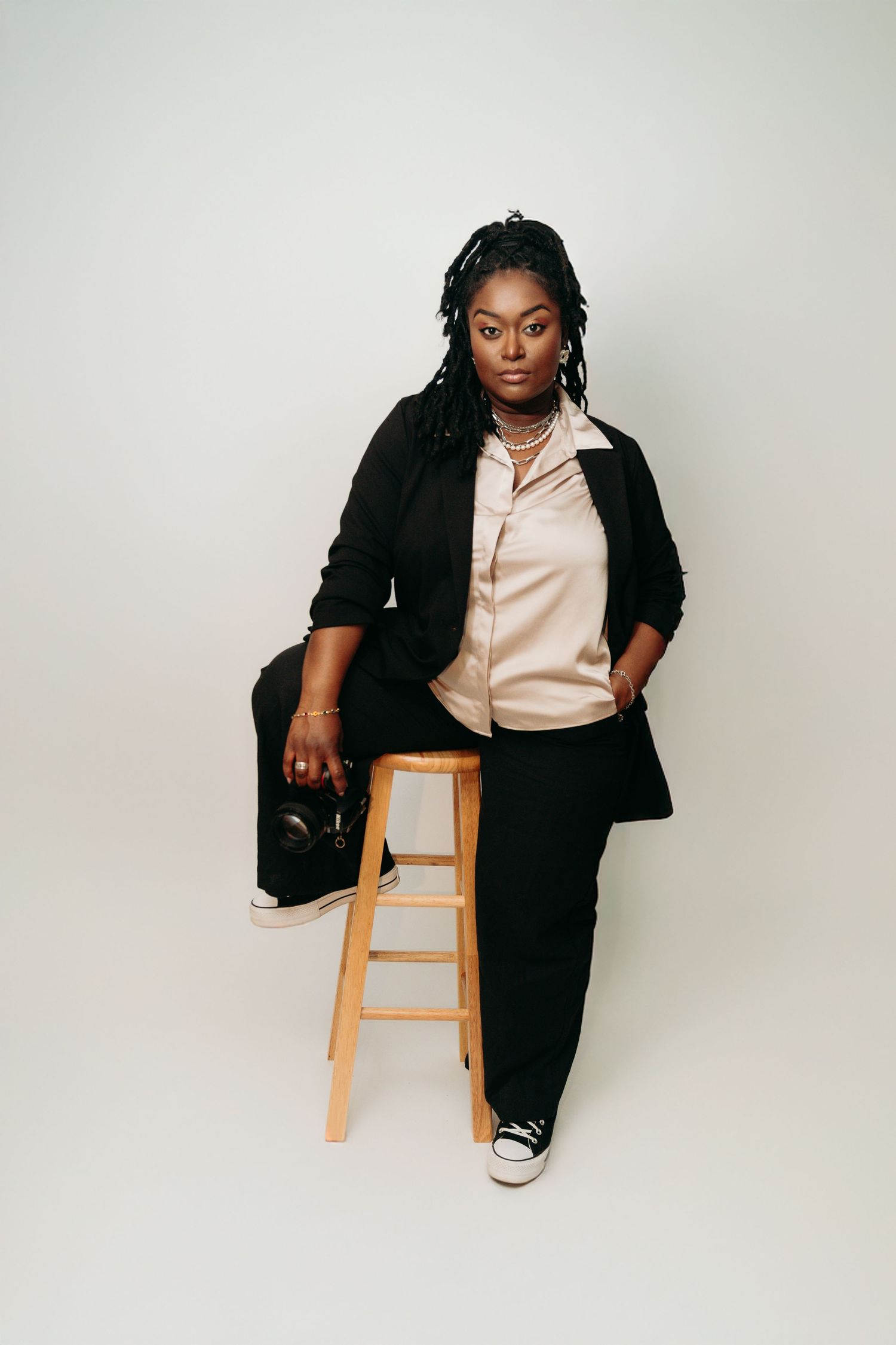 Professional studio photoshoot featuring casual business attire and wooden stool against white backdrop.