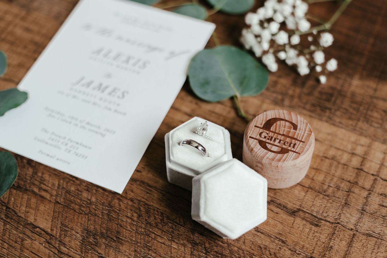 Wedding stationery details with greenery and white floral accents on wooden background.