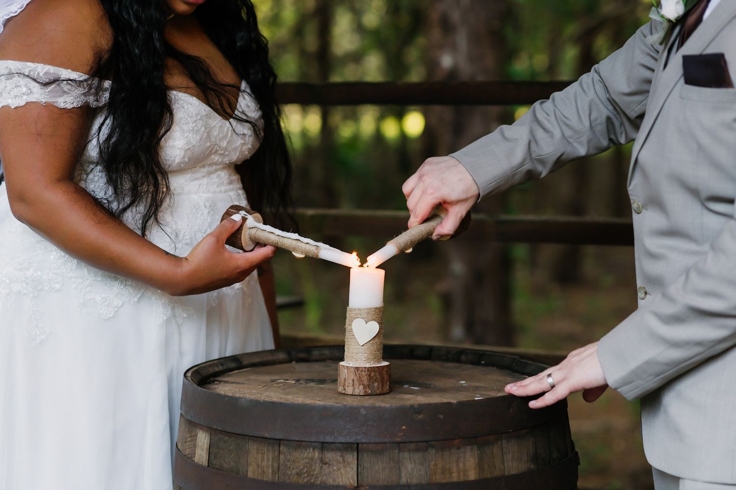 Couple's hands placing rings on rustic wooden barrel during outdoor ceremony.