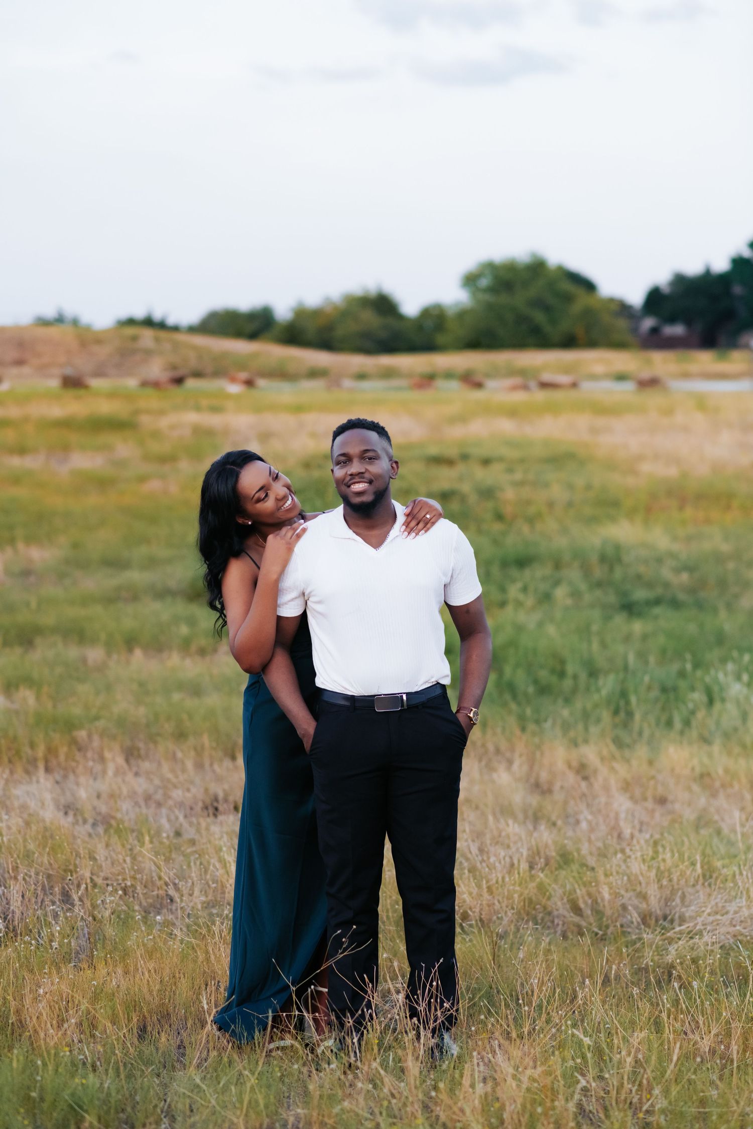 A couple poses together in a golden field during sunset.