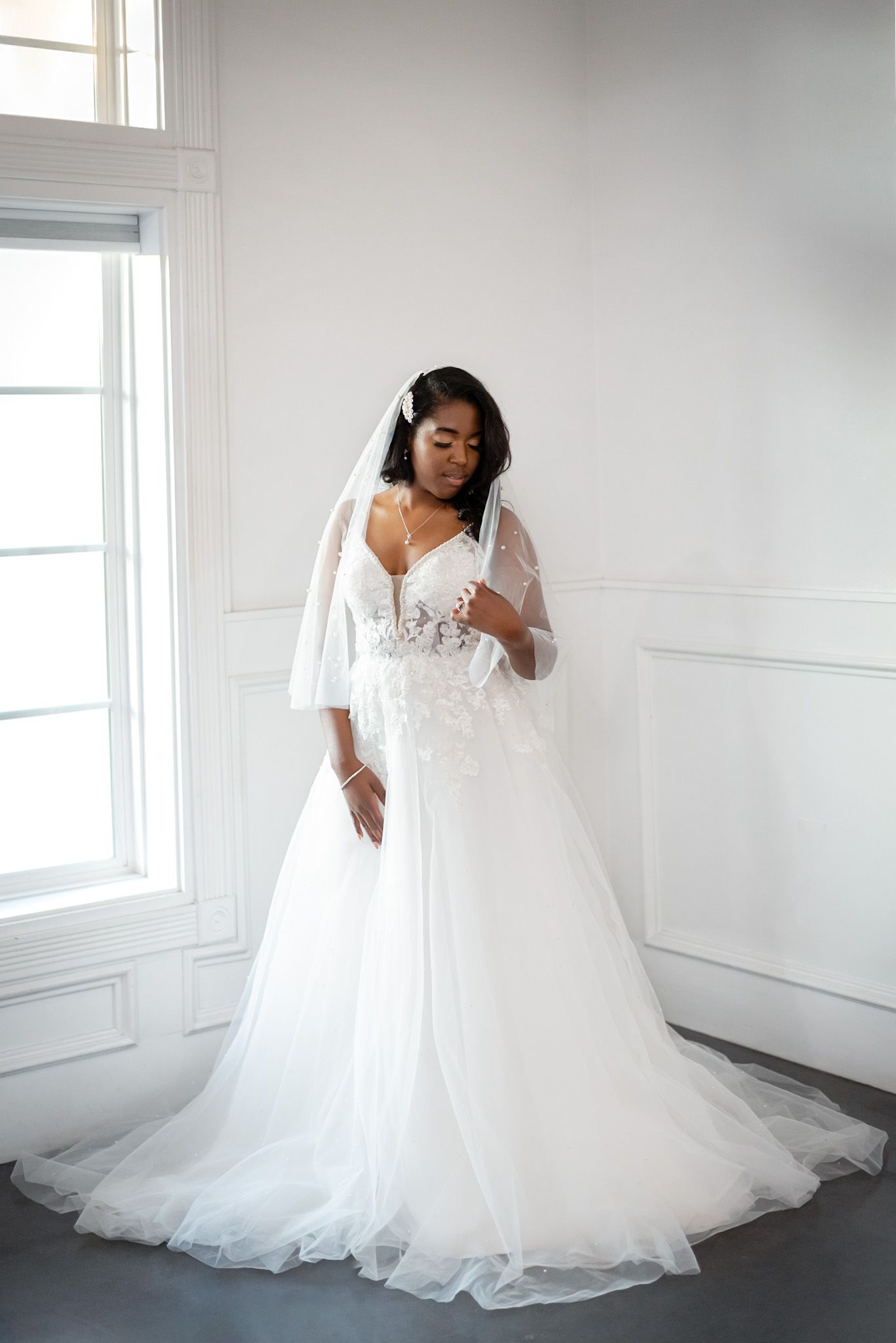 Elegant white wedding gown with lace details and flowing tulle skirt in bright room.