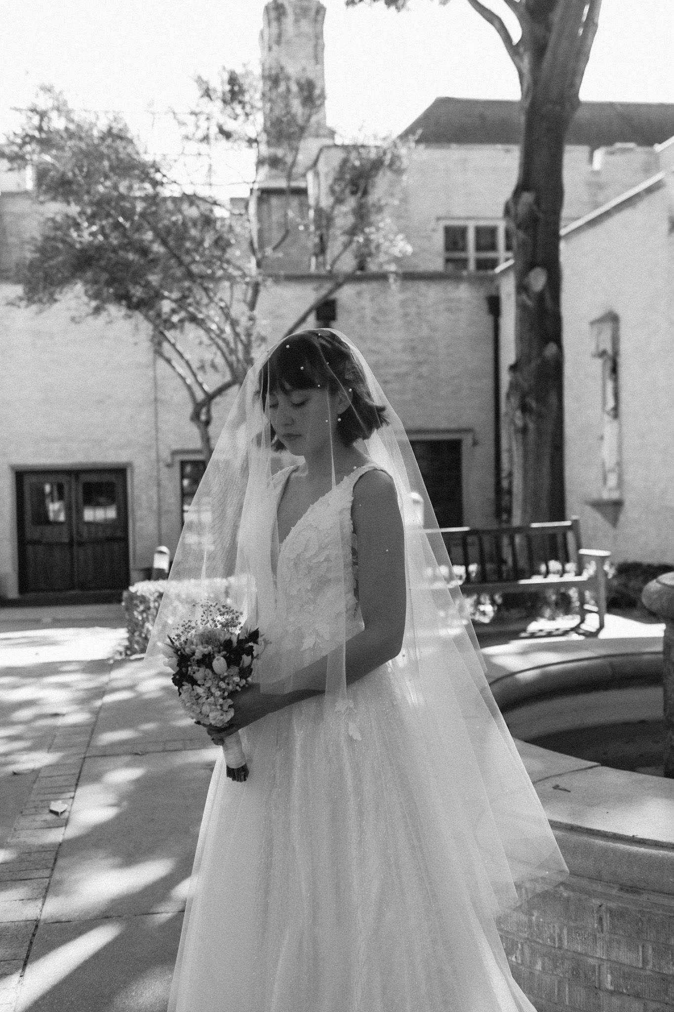 Bride in flowing white gown walking along sunny urban street.