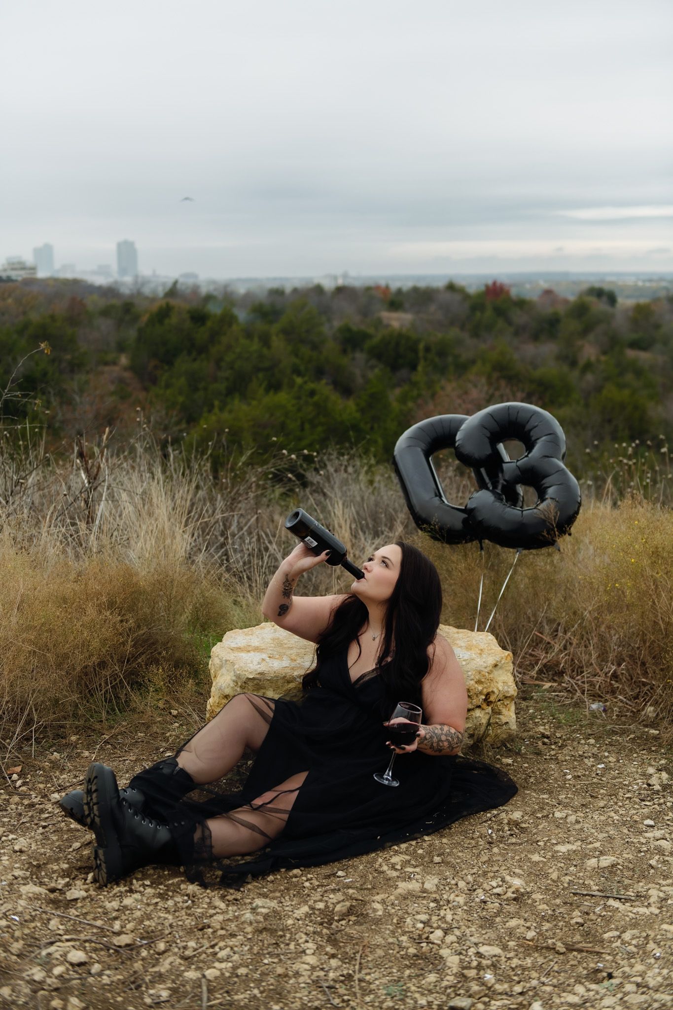 Figure lying on ground holding cake against cloudy sky and natural landscape.