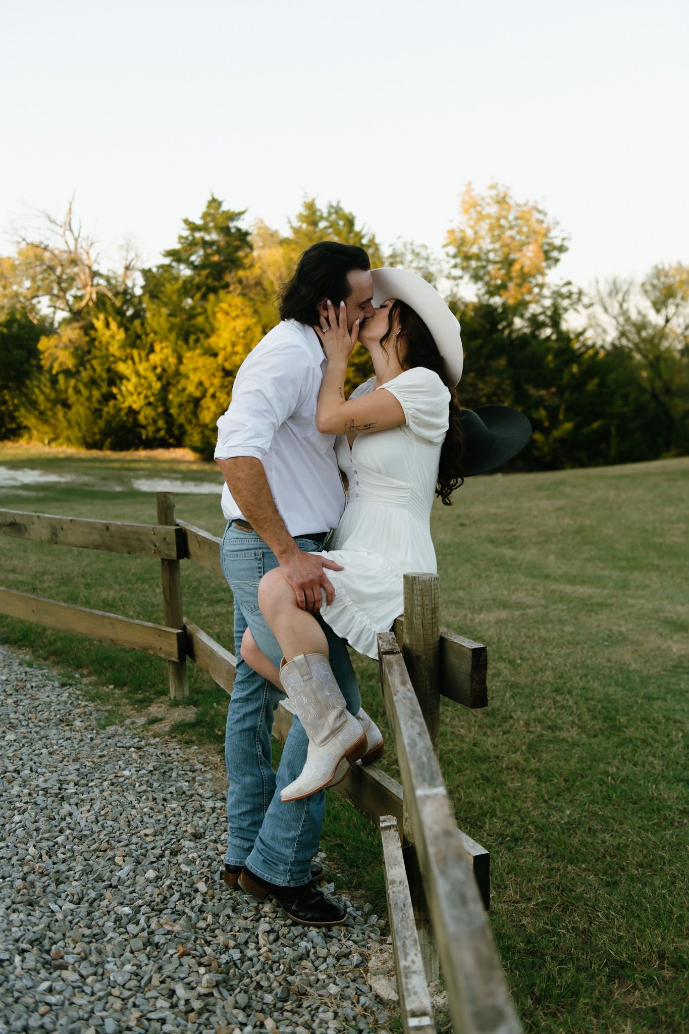 Romantic couple sharing intimate moments against a rustic wooden fence at sunset.