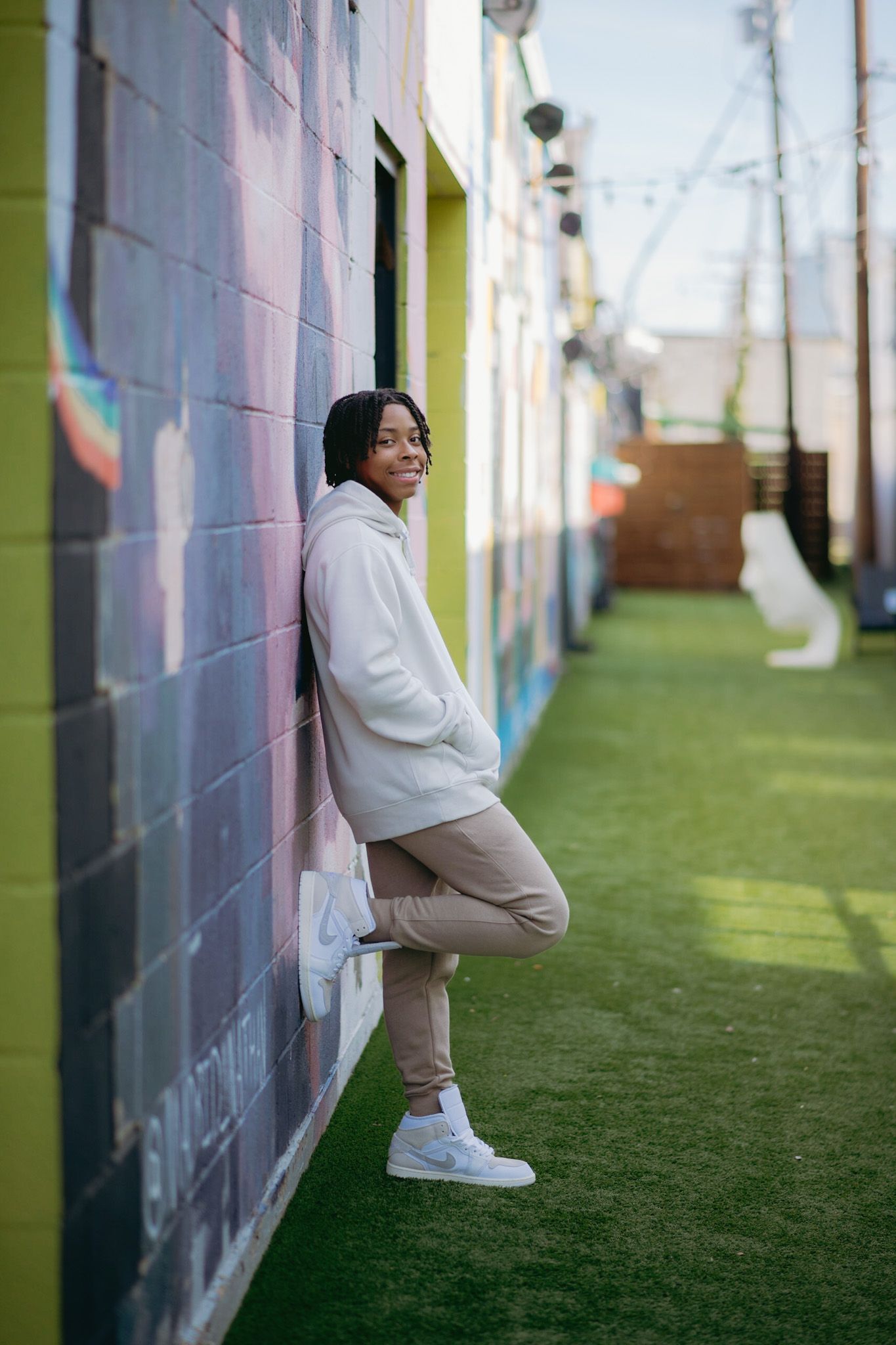 A person in casual wear leans against a vibrant painted wall with artificial turf ground.