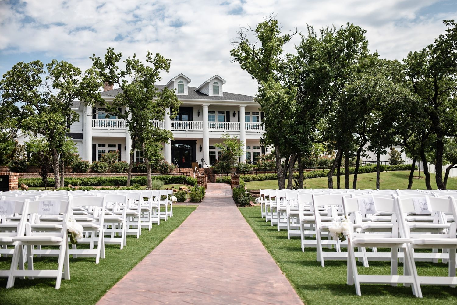 Outdoor wedding ceremony setup with rows of white chairs and tree-lined aisle.
