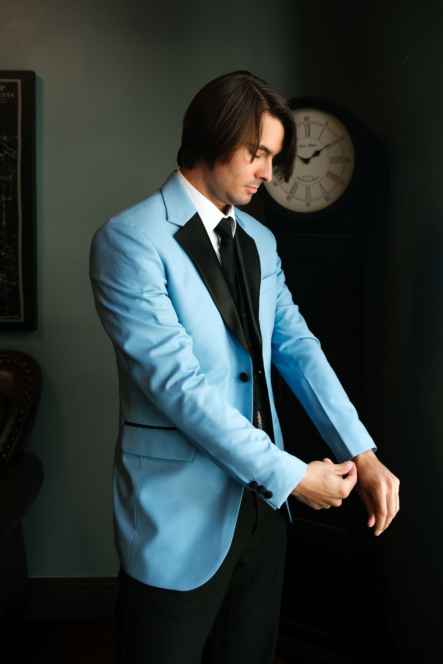 Stylish groom in light blue suit jacket preparing in moody lighting.