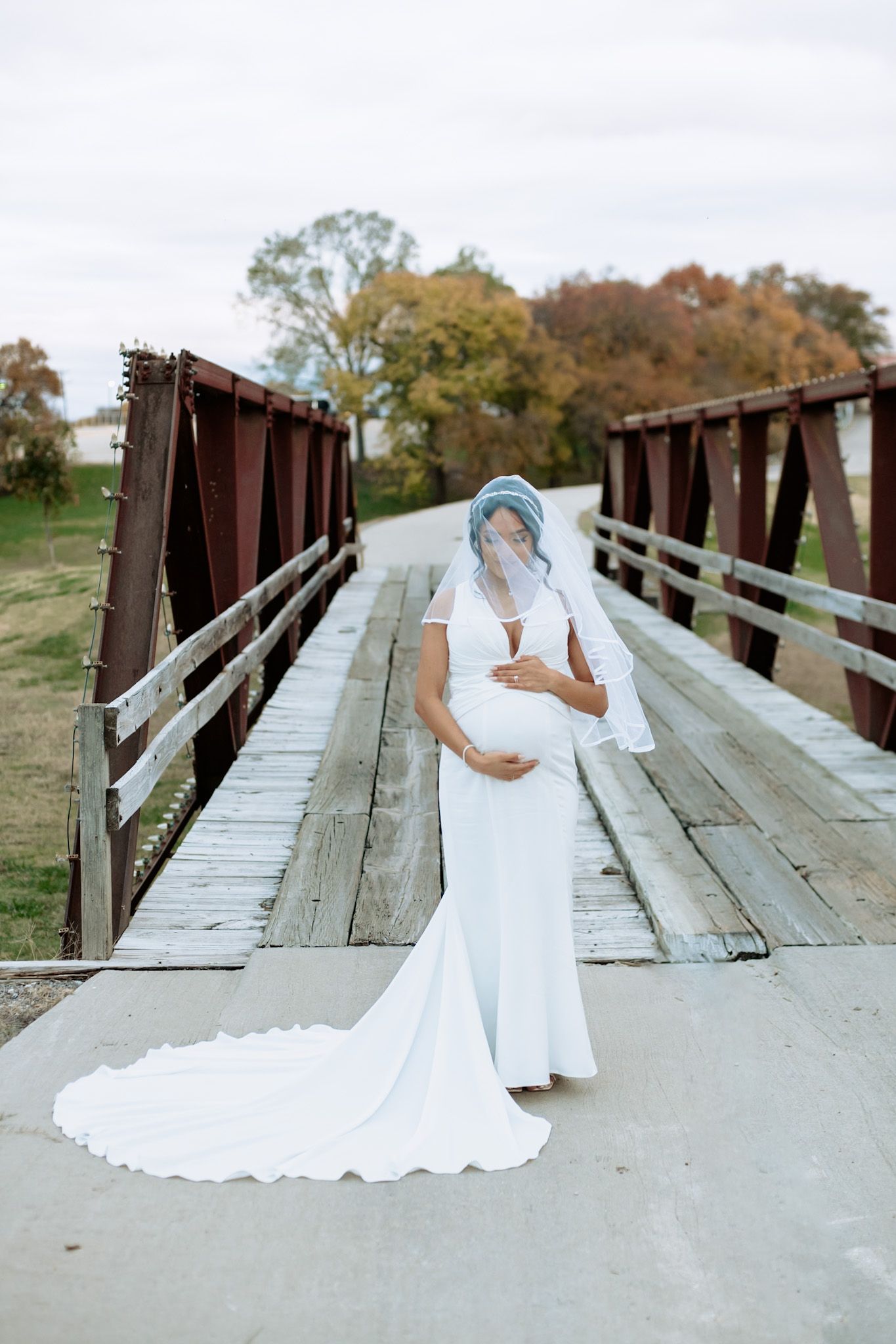 Bride in flowing white dress poses on rustic wooden bridge.