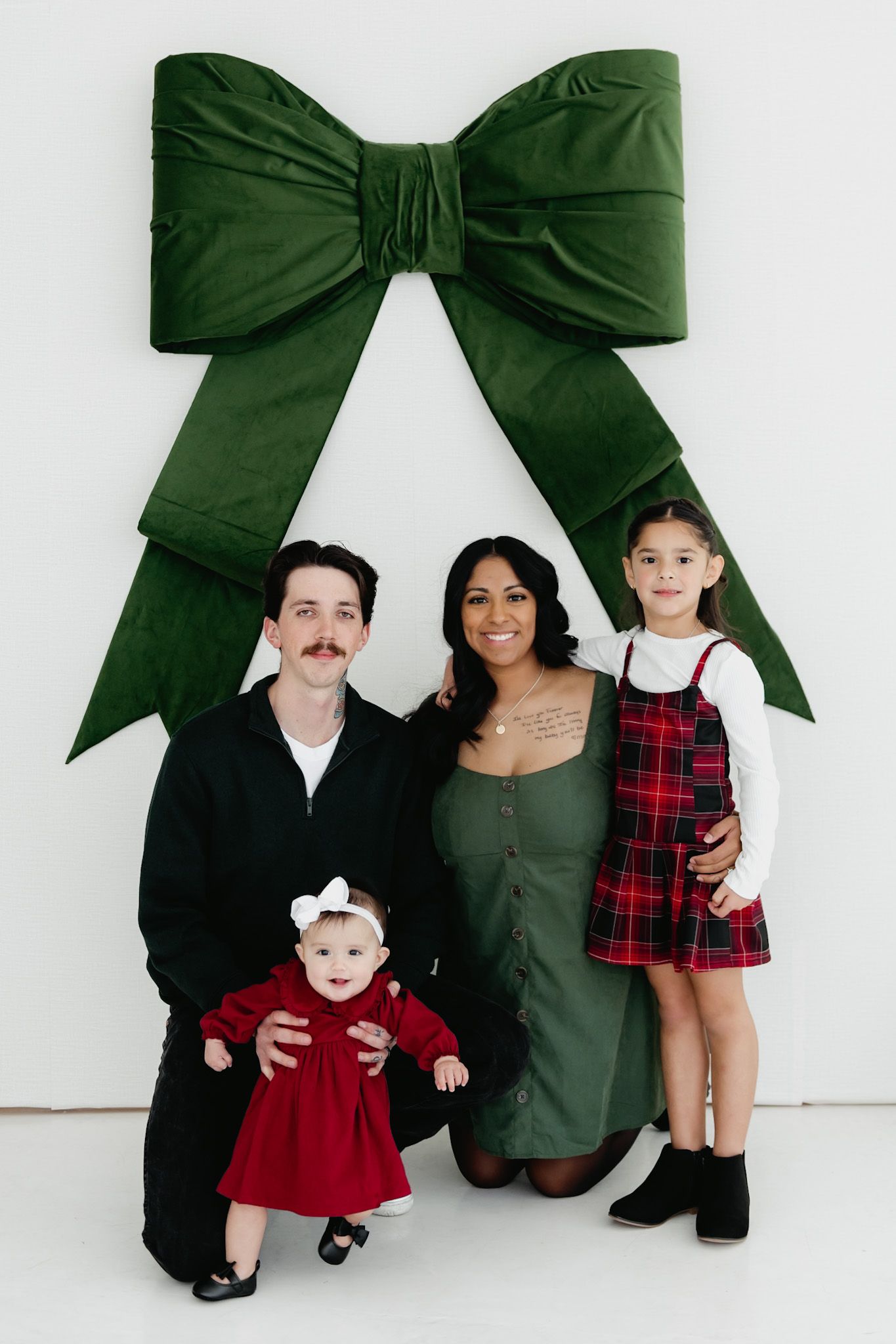 A family poses for a holiday portrait under a large green bow decoration.