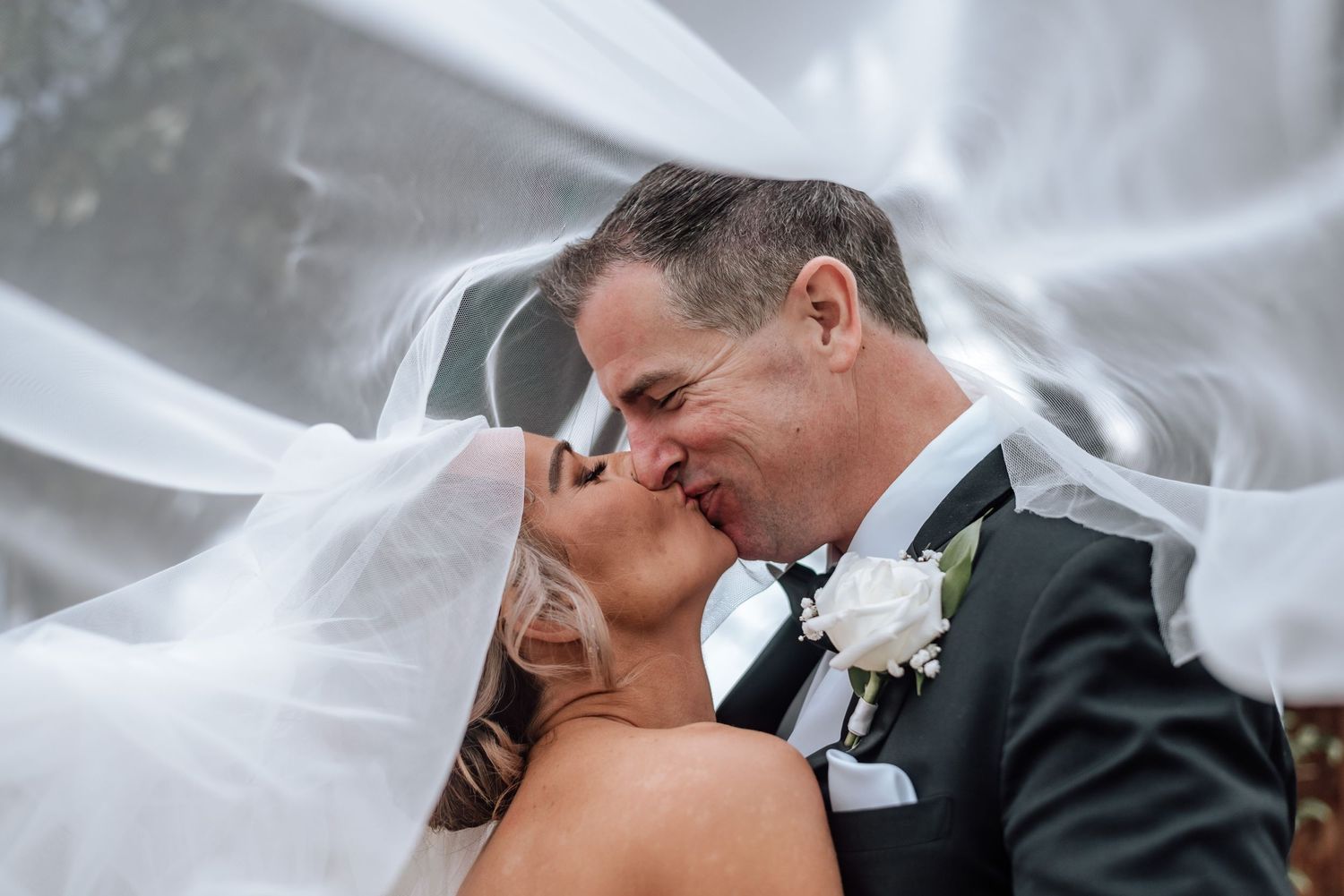 Intimate wedding couple moment captured through delicate white veil outdoors.