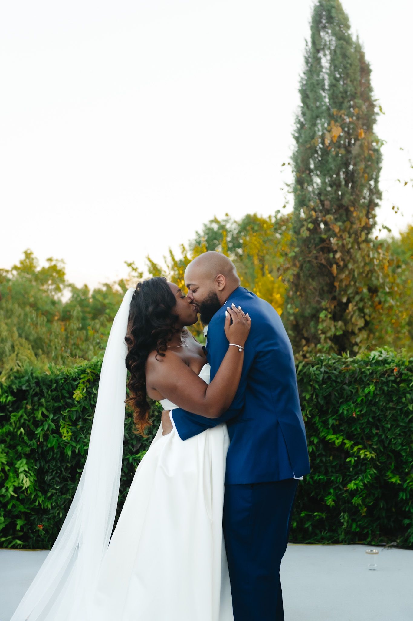 Romantic outdoor wedding portraits against lush garden backdrop at sunset.