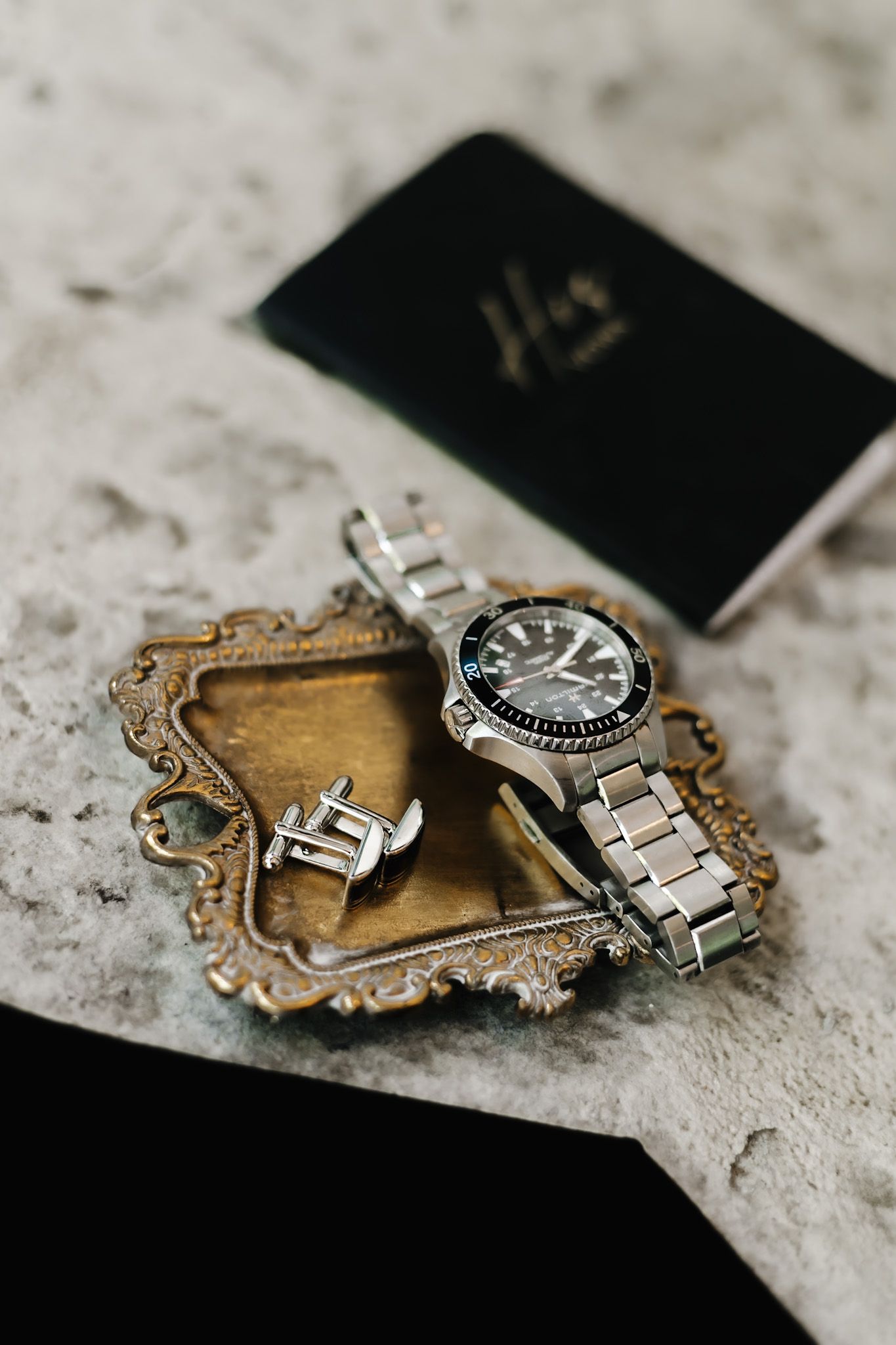 A luxury watch and wedding rings displayed on an ornate gold tray with a black passport.