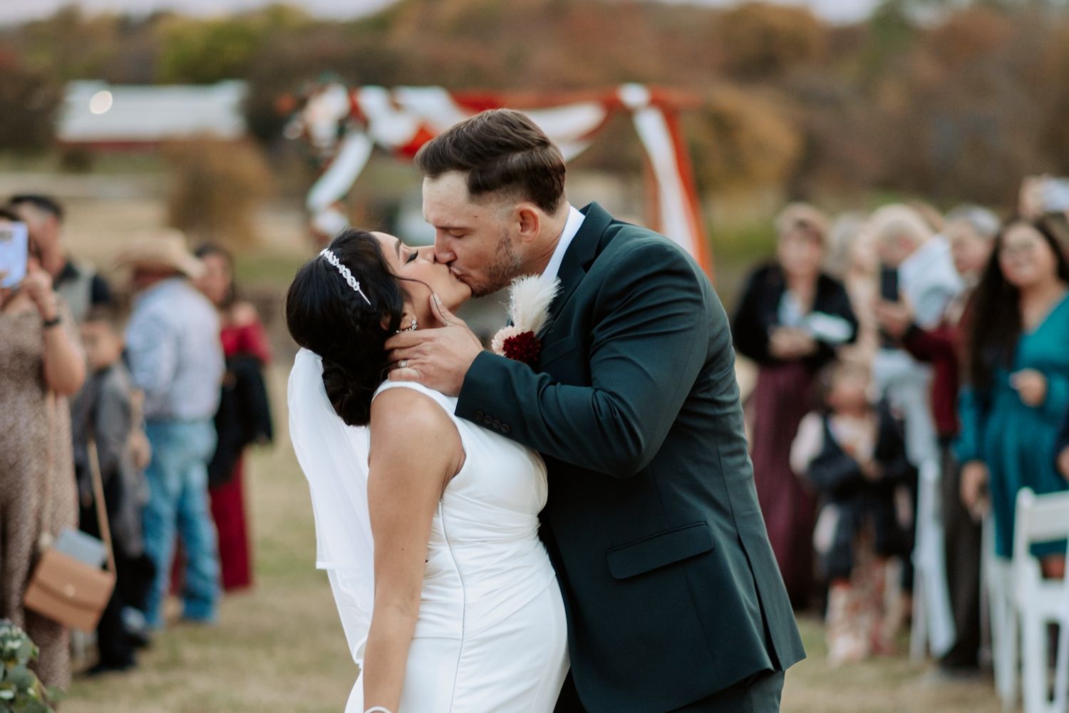 Wedding ceremony kiss captured outdoors with guests in background.