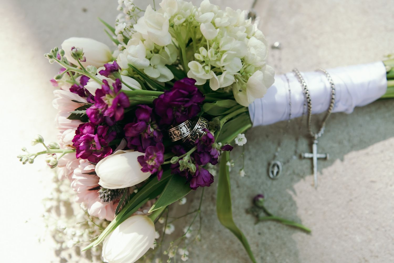 Wedding bouquet with white tulips and purple flowers against light background.
