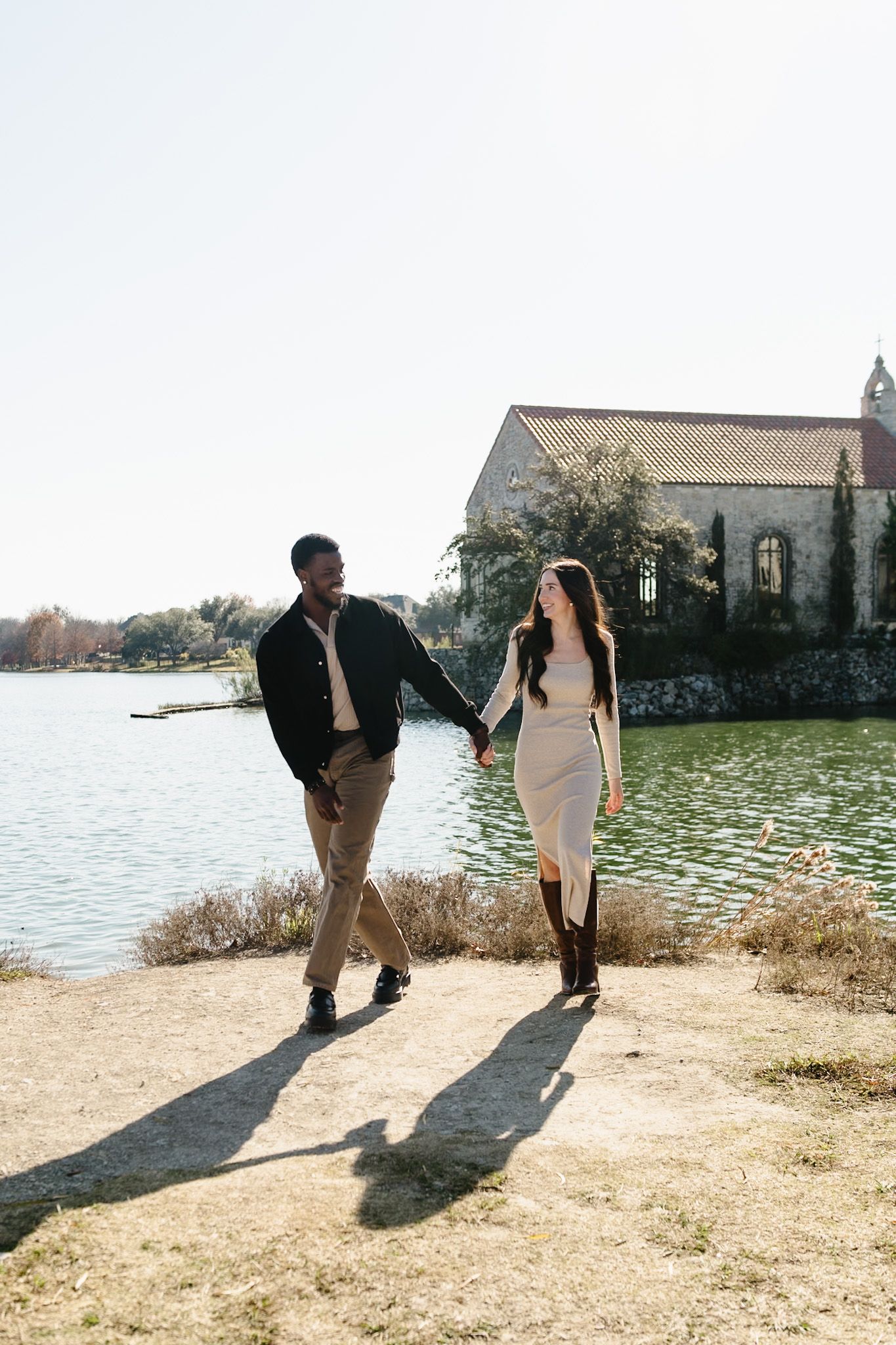 A couple walks along a waterfront path with historic buildings in the background.