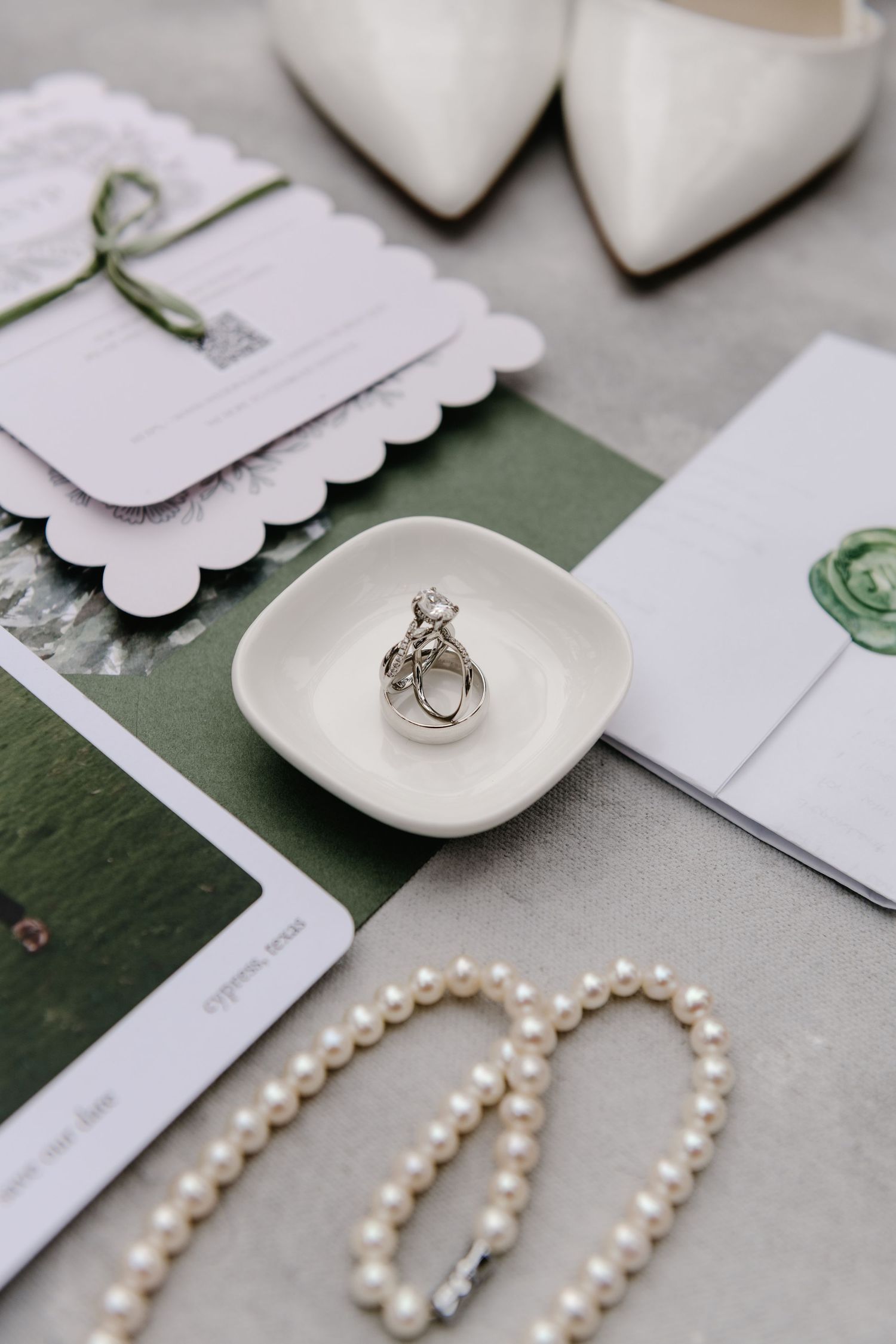 Pearl necklace and wedding rings displayed with white stationery and accessories.