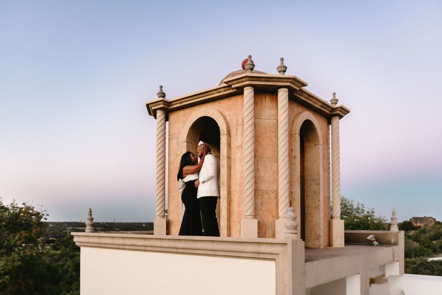 Couple poses dramatically at historic stone architecture during golden hour.