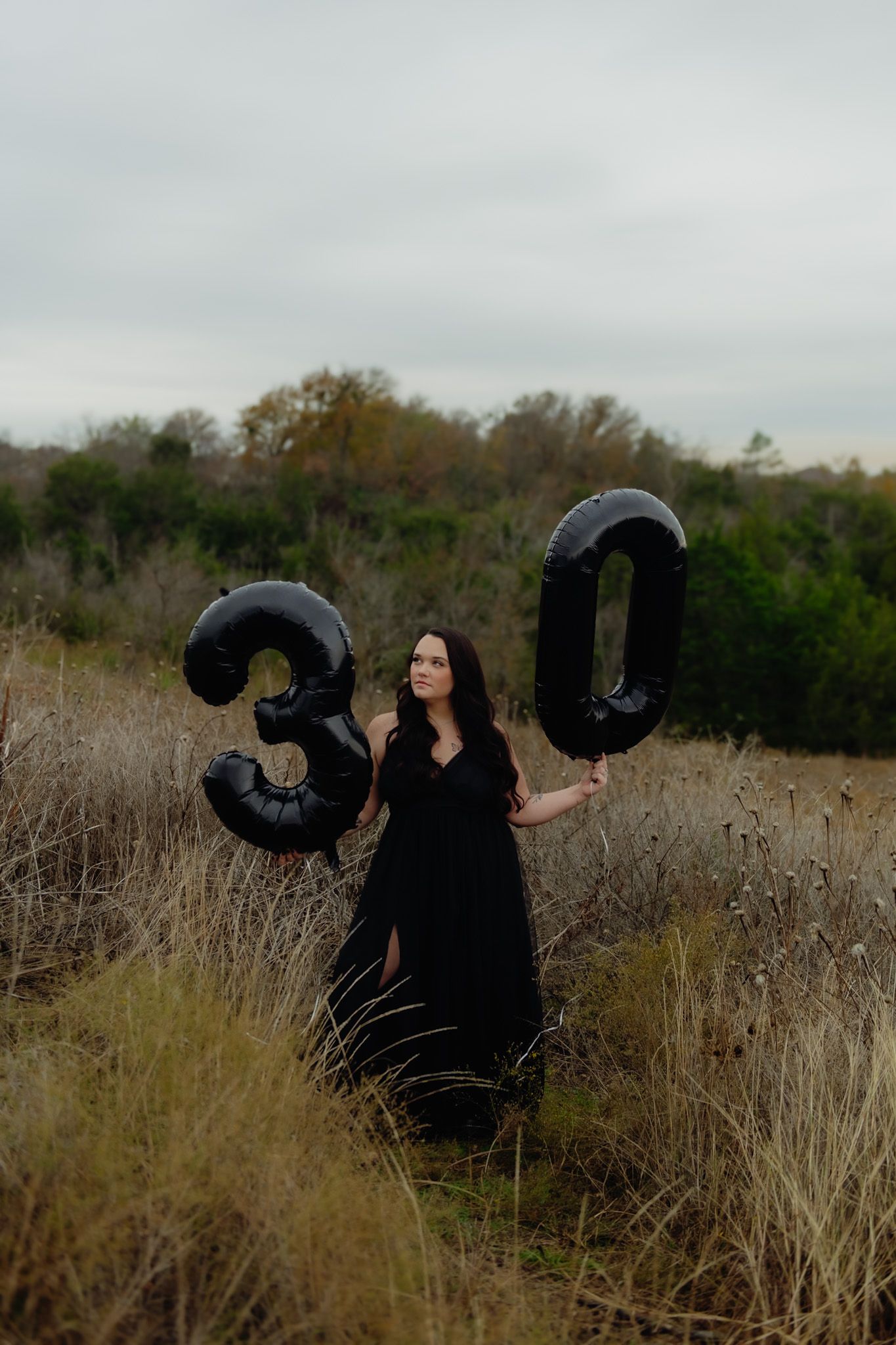 Person in black outfit dancing with balloons in outdoor field setting.