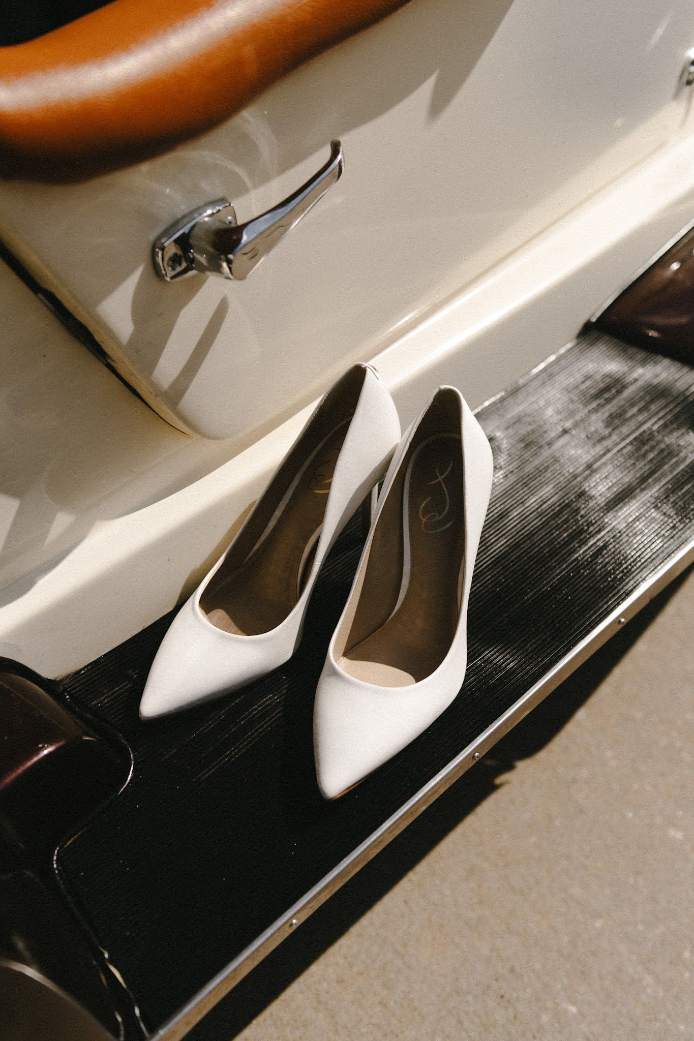White pointed-toe bridal shoes arranged on a dark surface with dramatic lighting.