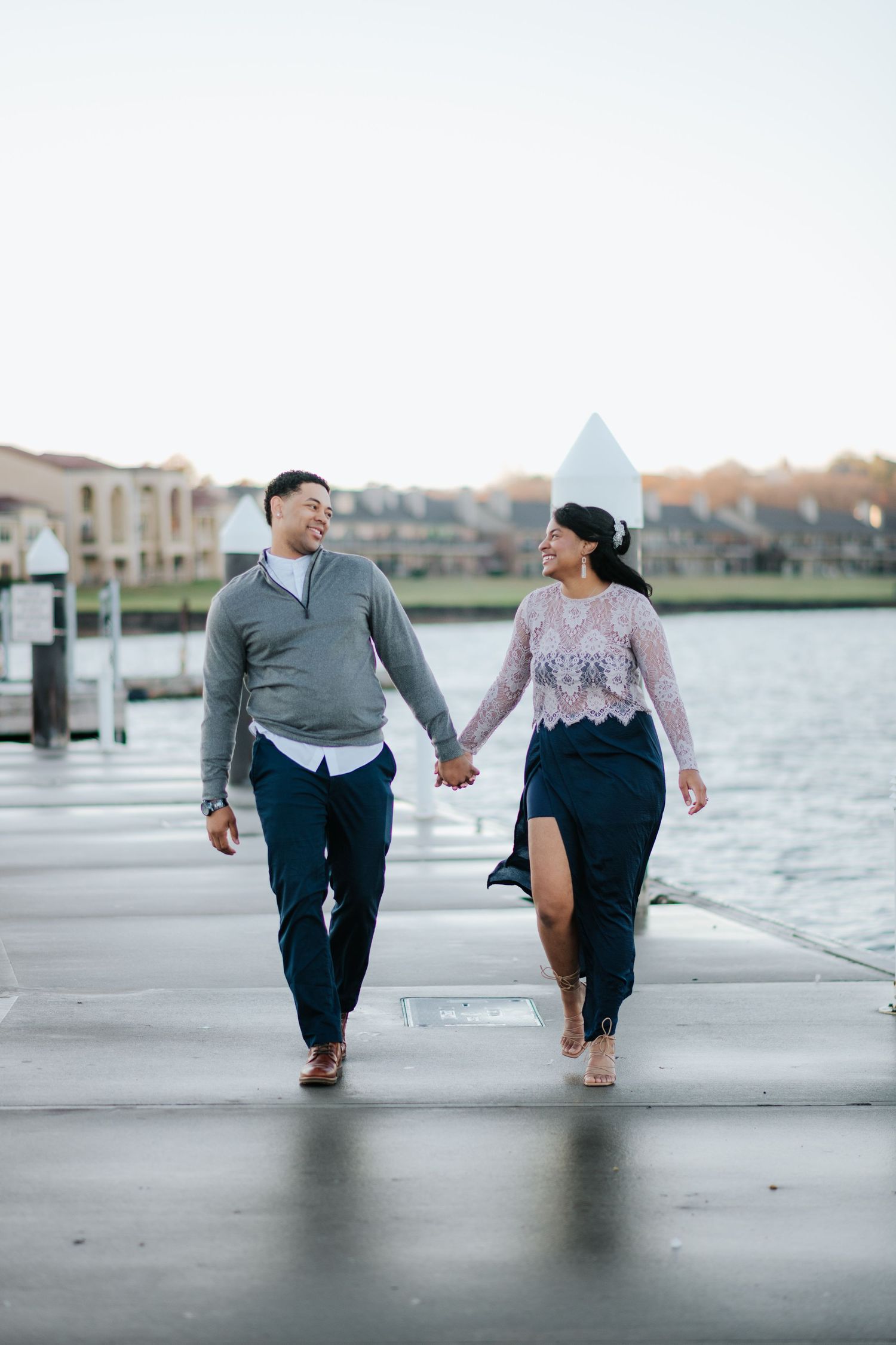 Couple runs playfully along waterfront pier with lighthouse in background.