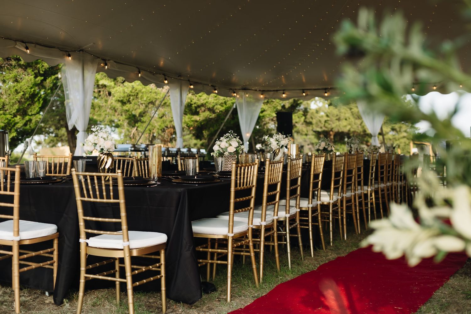 Wedding venue setup with rows of chairs and red carpet under outdoor tent.