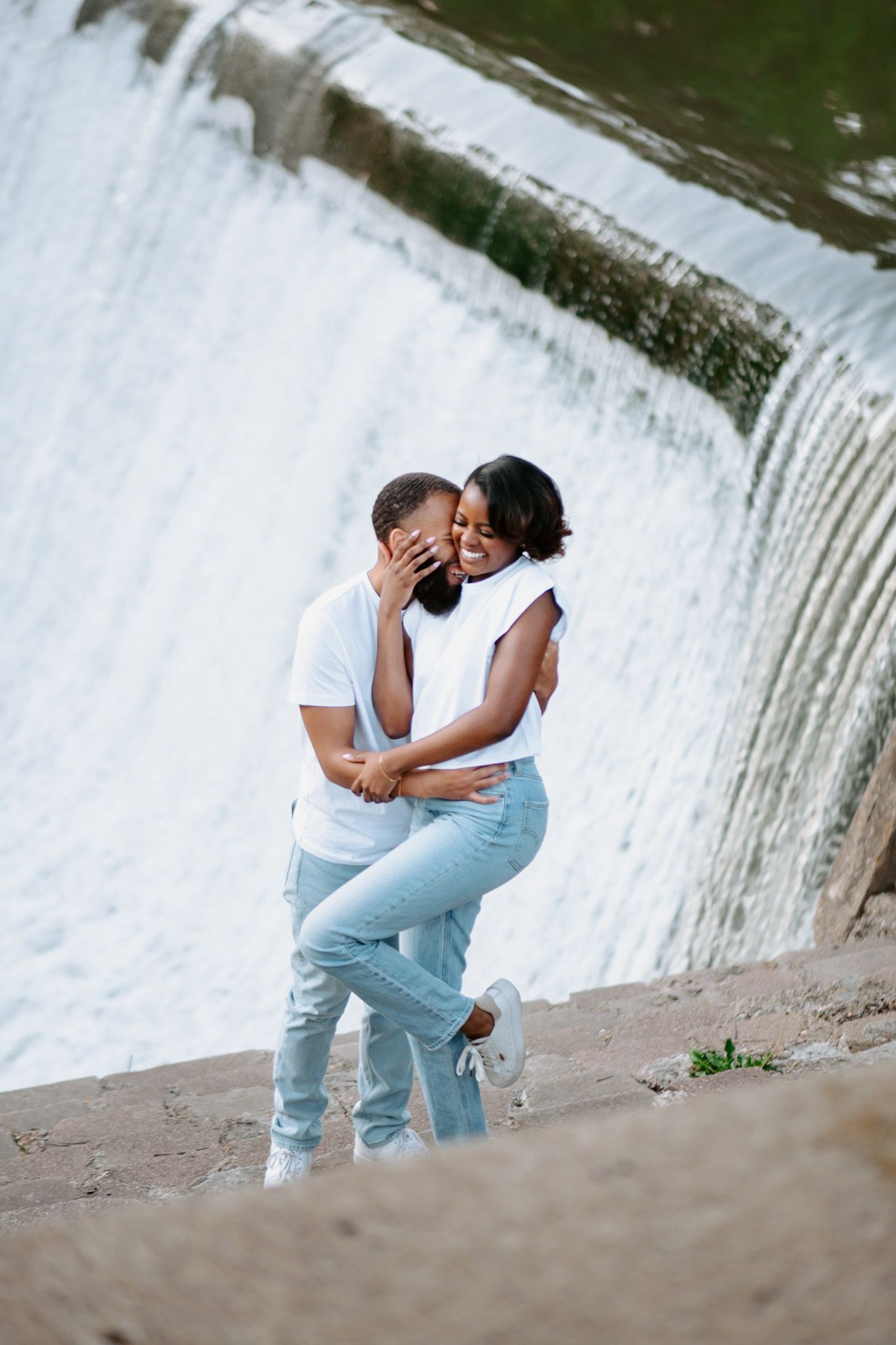 Romantic couple poses near a cascading waterfall in coordinated white and blue outfits.