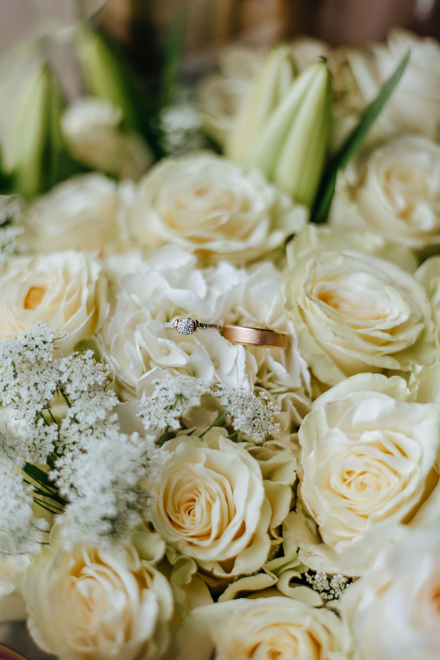 White roses and baby's breath bouquet with wedding rings nestled among flowers.
