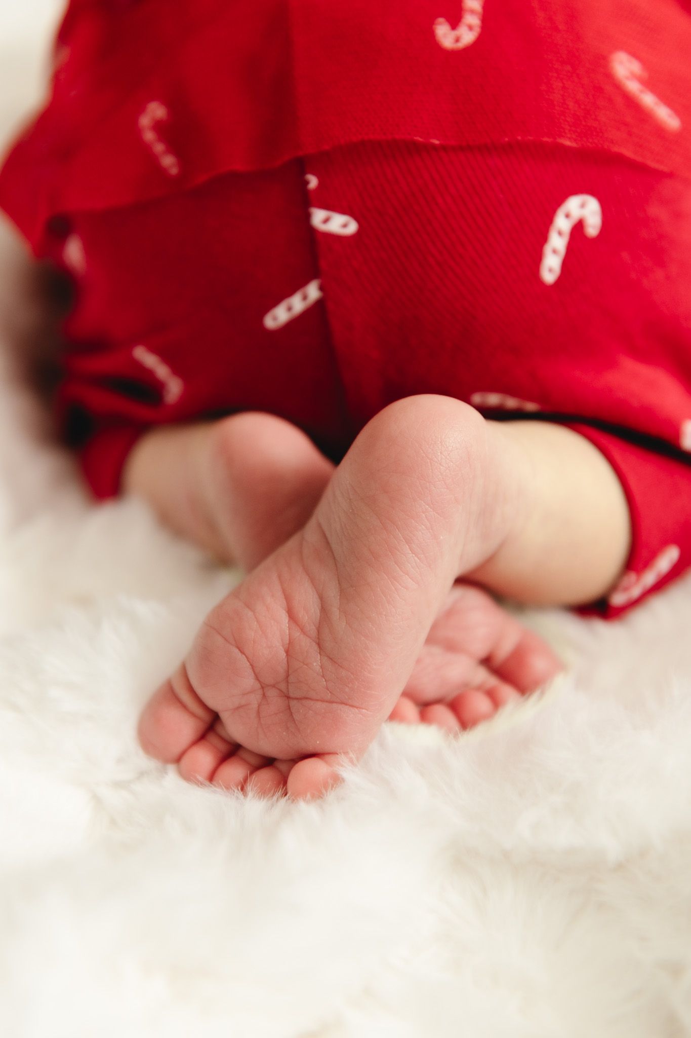 Close-up of tiny baby feet against white fabric with candy cane pattern.