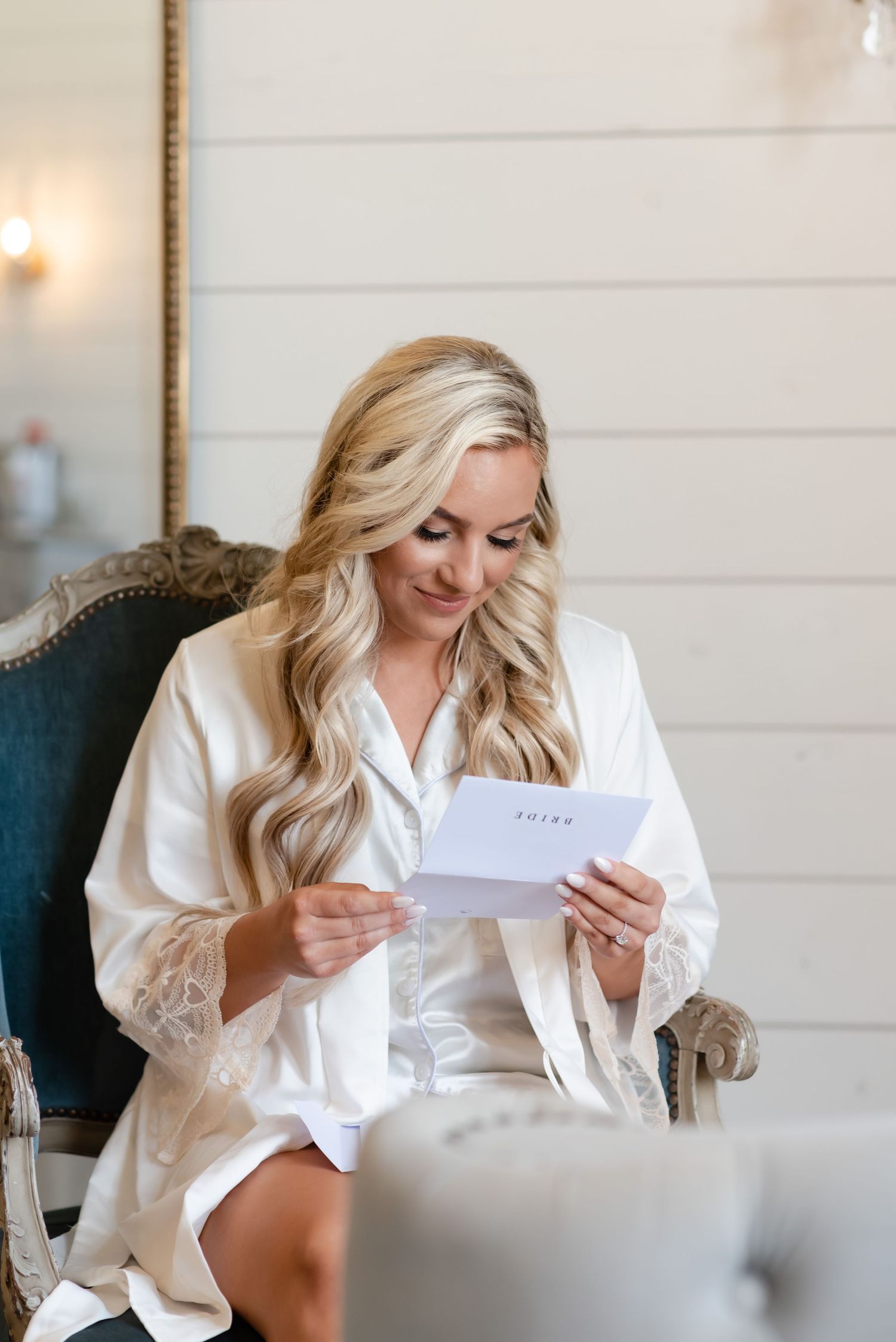 Someone in white robe reading letter while sitting in elegant chair.