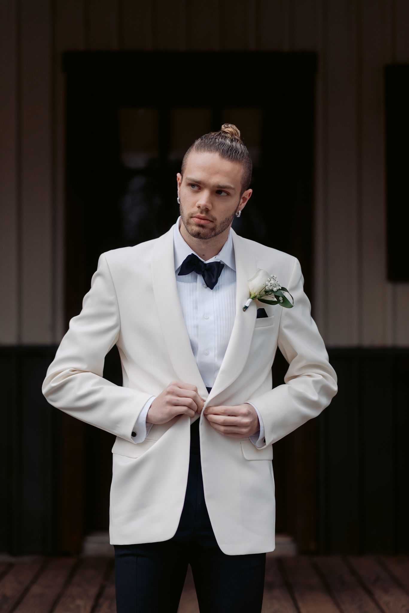 A groom in a white tuxedo jacket and black bow tie adjusts his buttons before the ceremony.