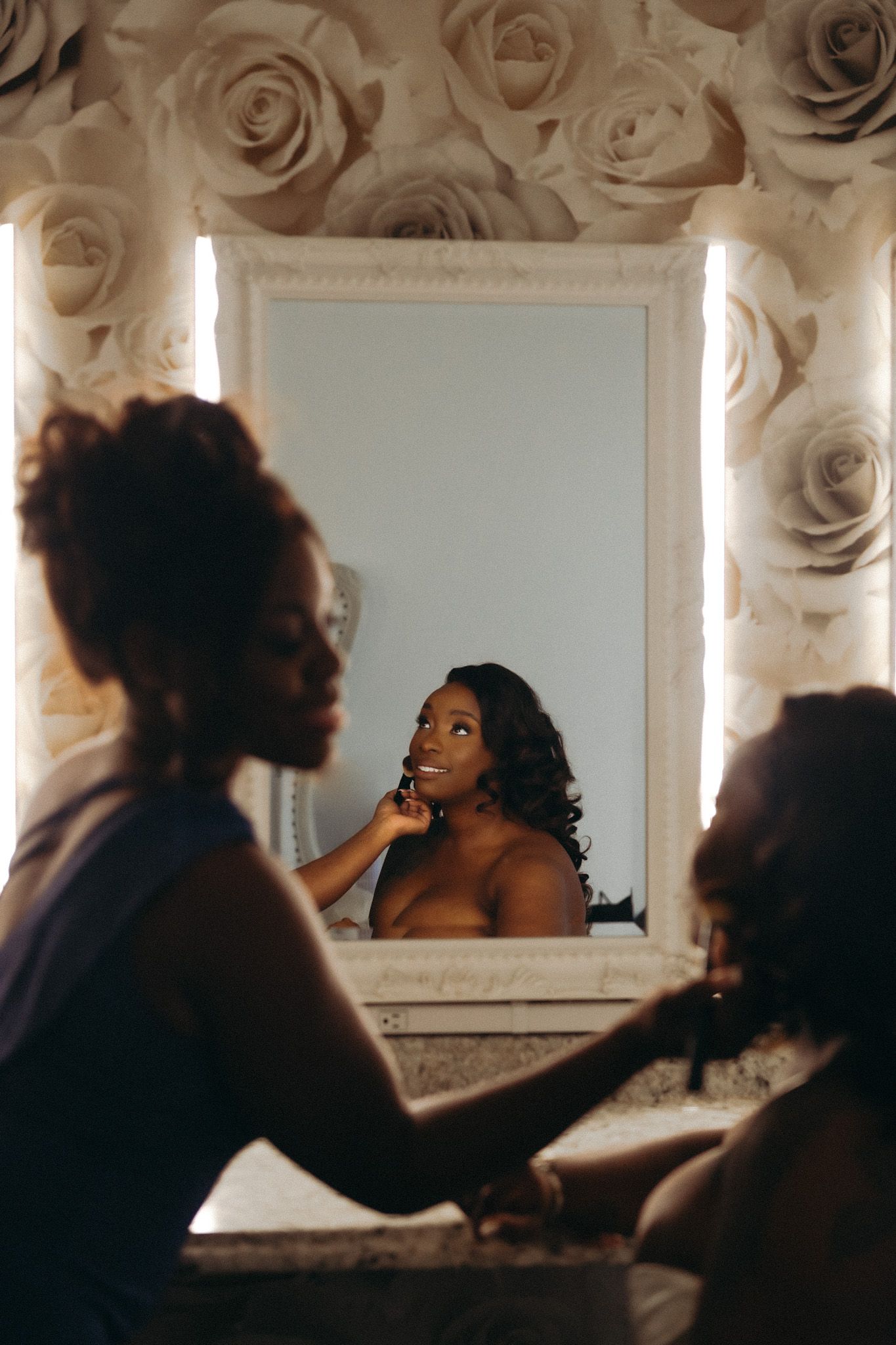 A series of silhouetted figures applying makeup in front of a mirror with soft rose petal background.