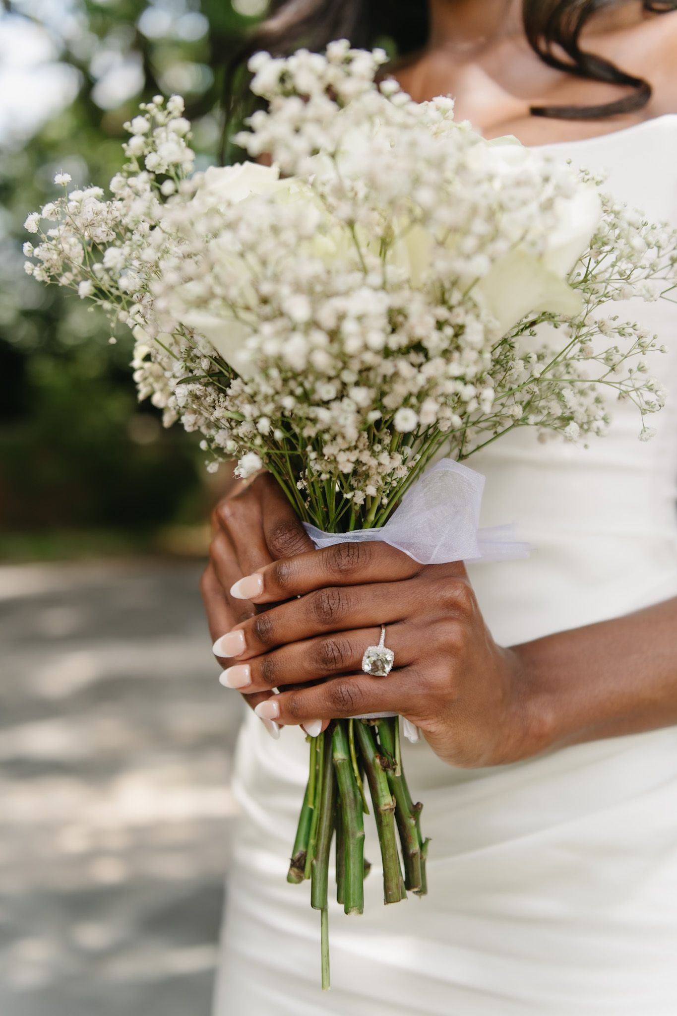 Close-up of hands holding a delicate baby's breath wedding bouquet with a sparkling engagement ring.
