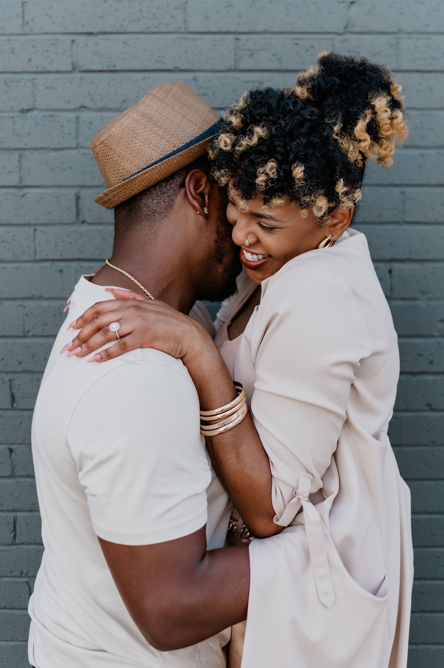 Intimate couple portrait against grey brick wall in soft pastel outfits.
