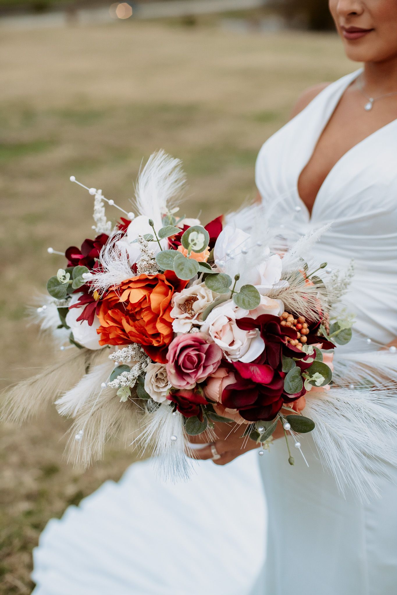 Elegant bridal bouquet with red and pink roses, feathers, and greenery.