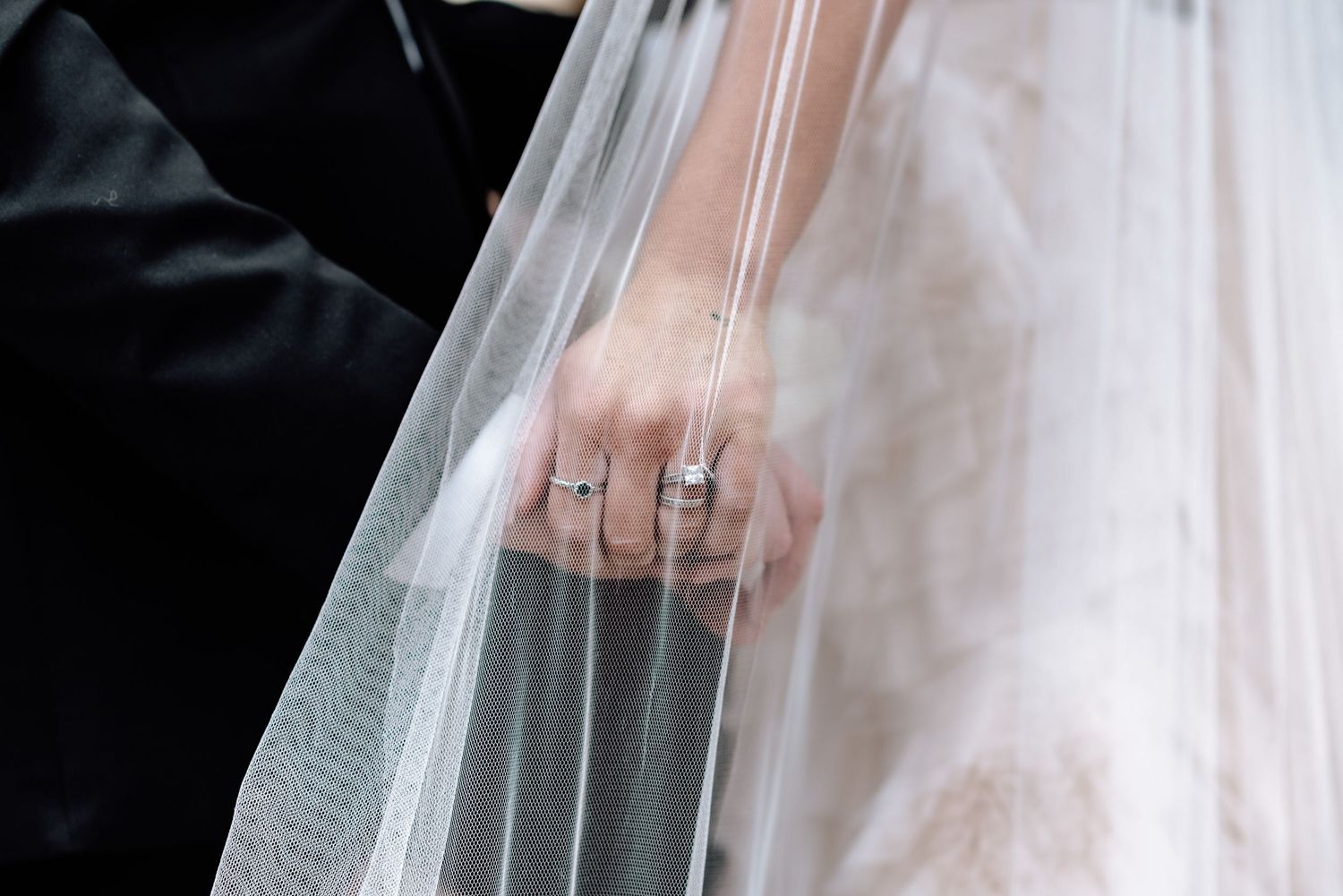 Romantic wedding couple embracing under flowing white veil during outdoor photo session.