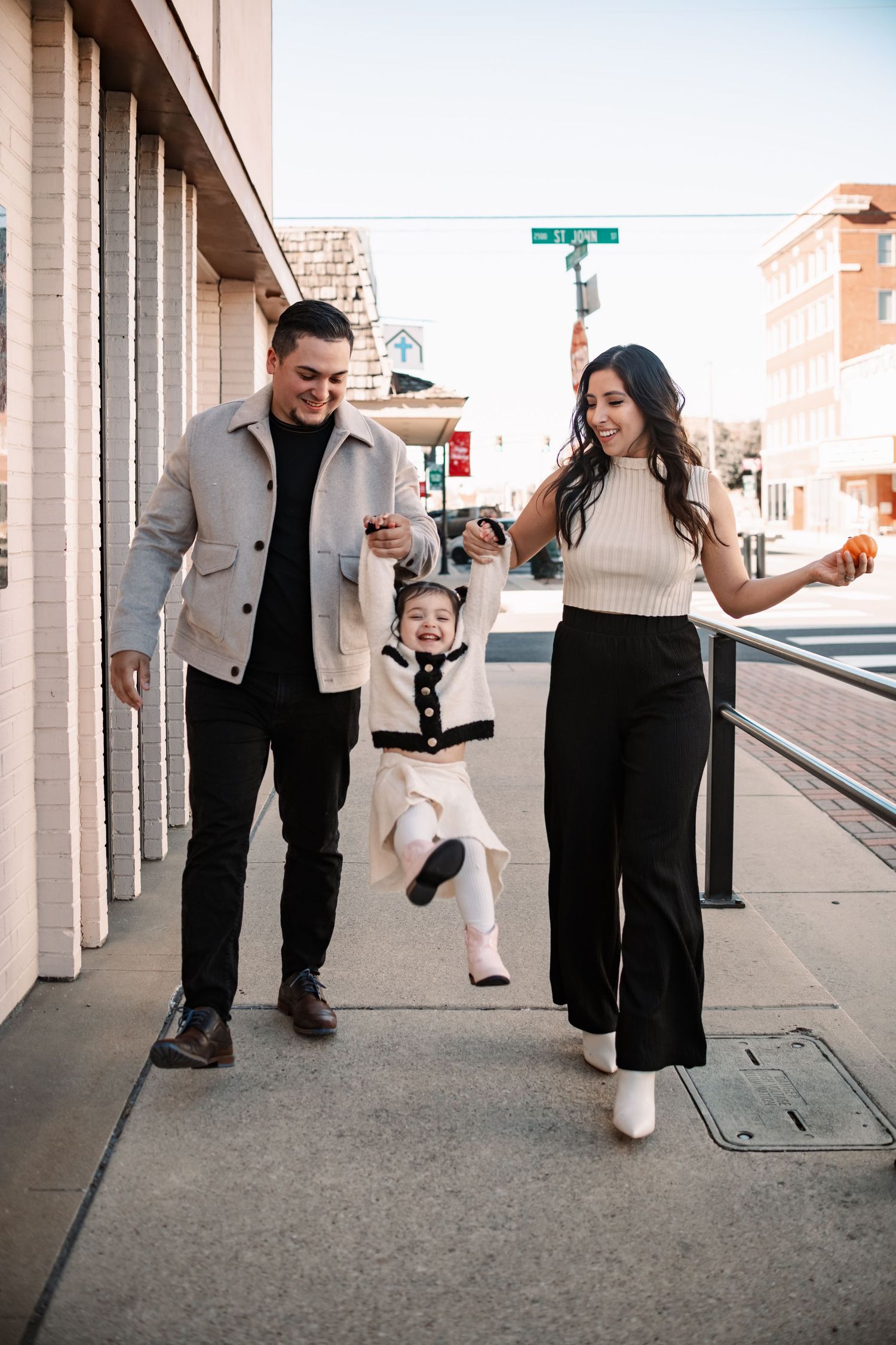 Family walking and playing together on urban sidewalk in black and white outfits.
