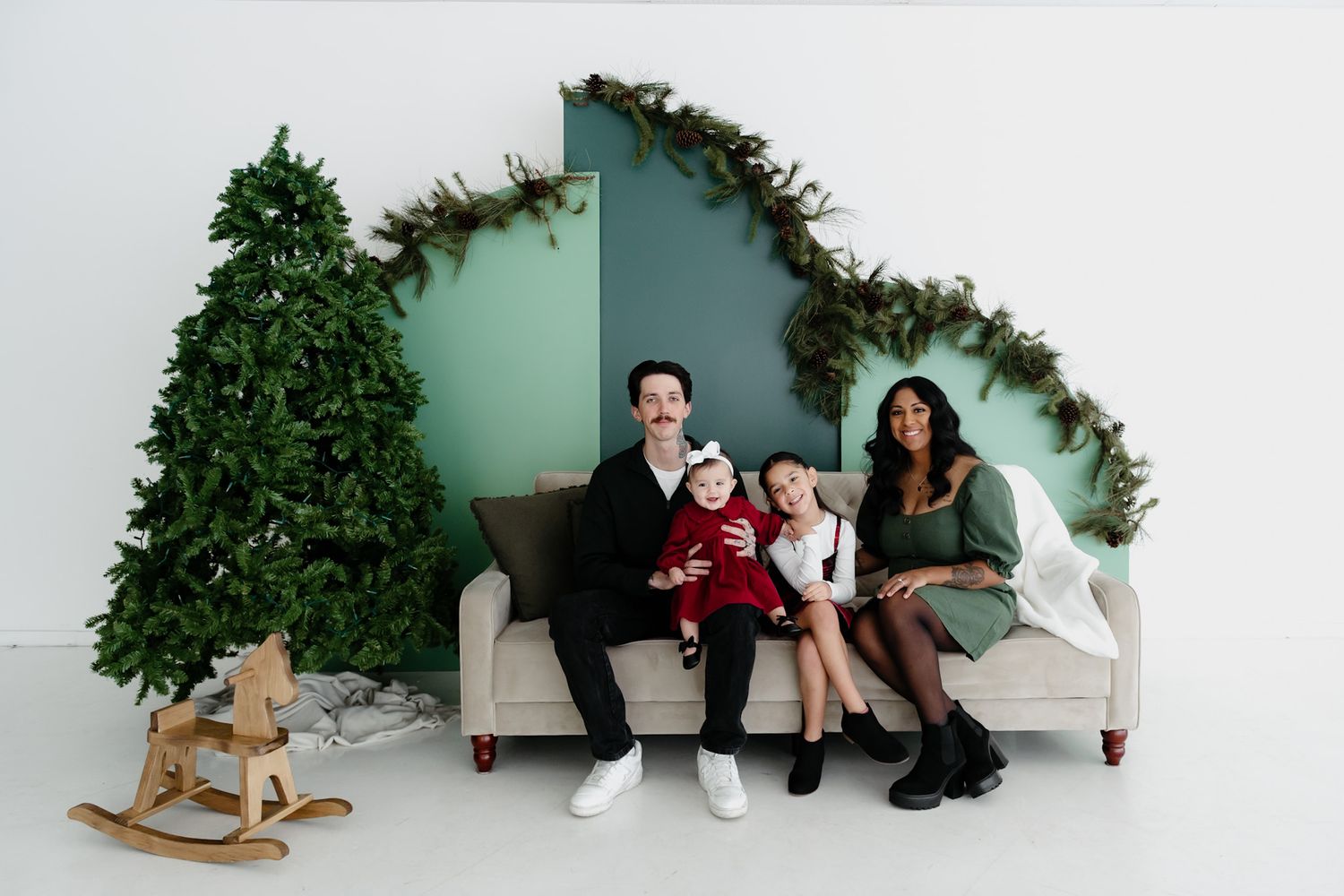 A family poses on a white couch with Christmas decorations and a rocking horse.