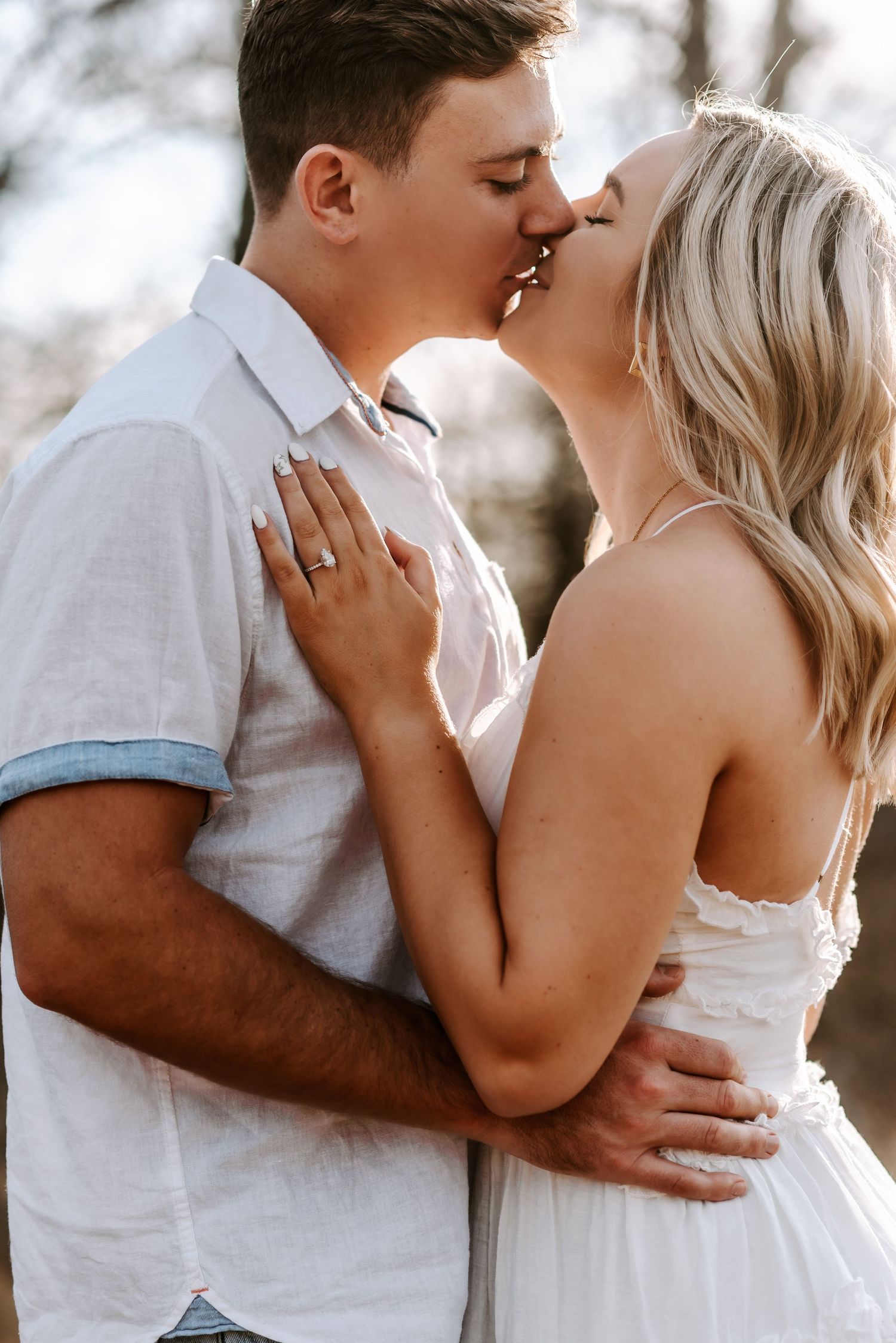 A couple shares an intimate moment in white outfits against a bright background.