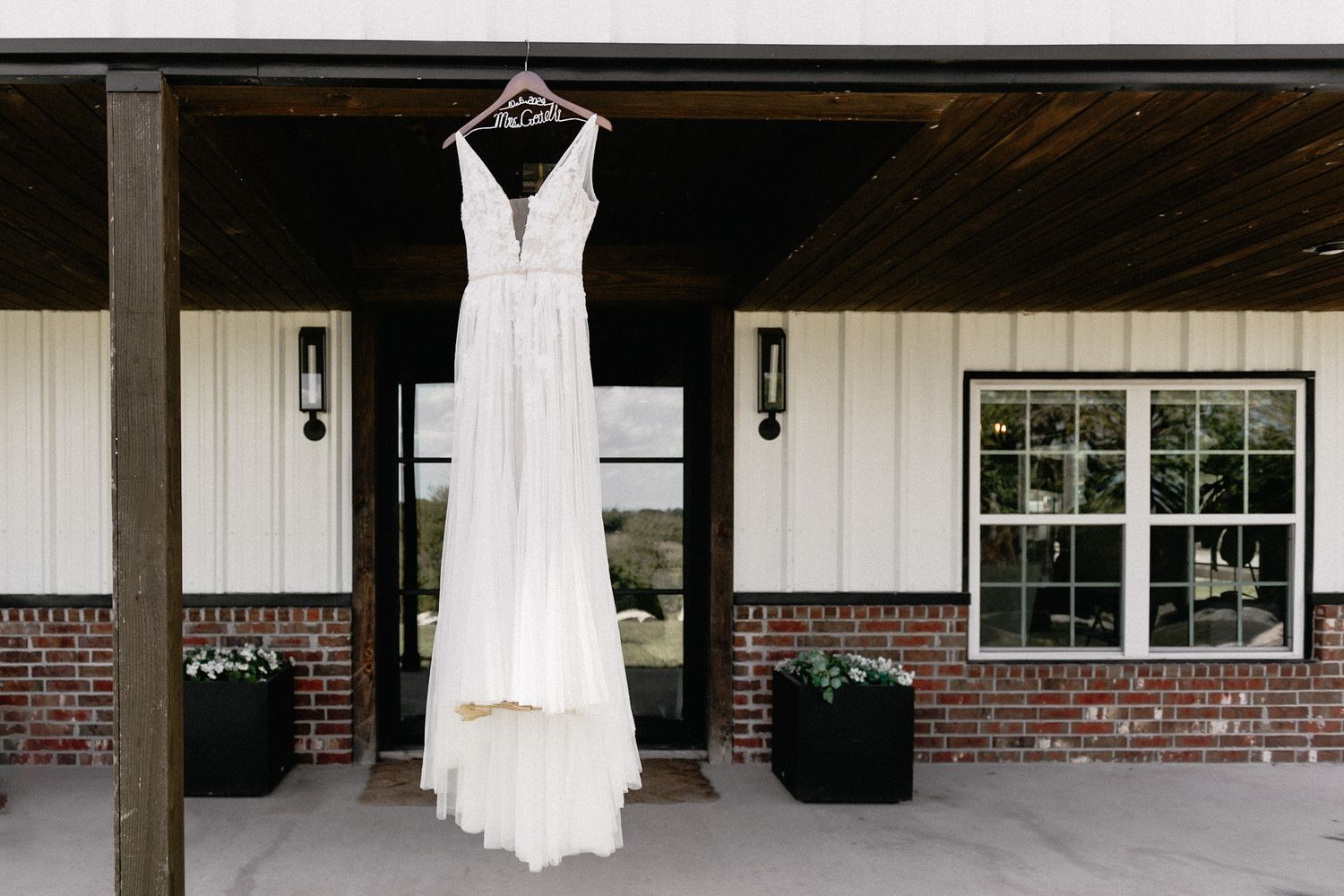 White wedding dress hanging on rustic barn wall exterior.