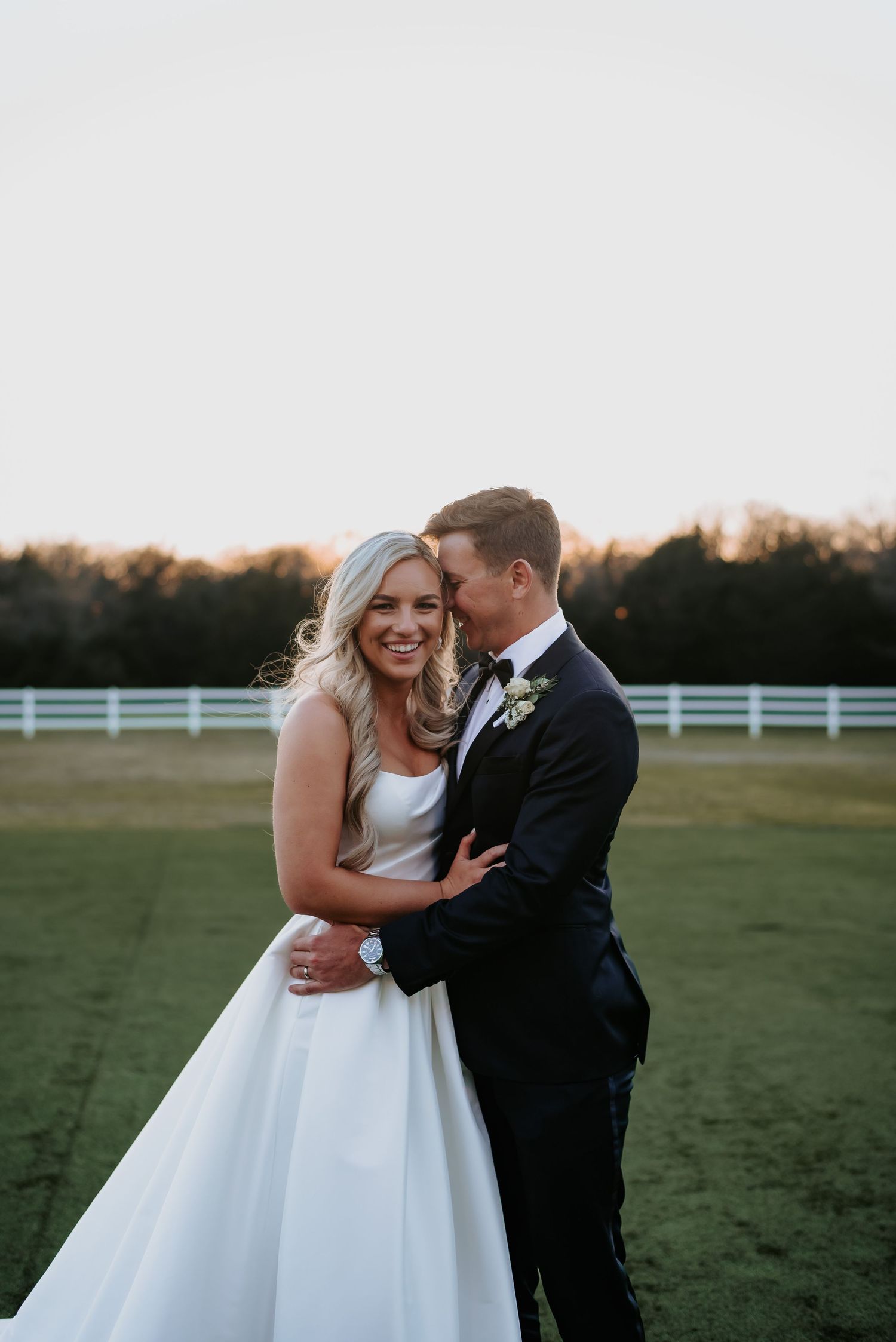Wedding couple sharing joyful moments in a field at sunset.