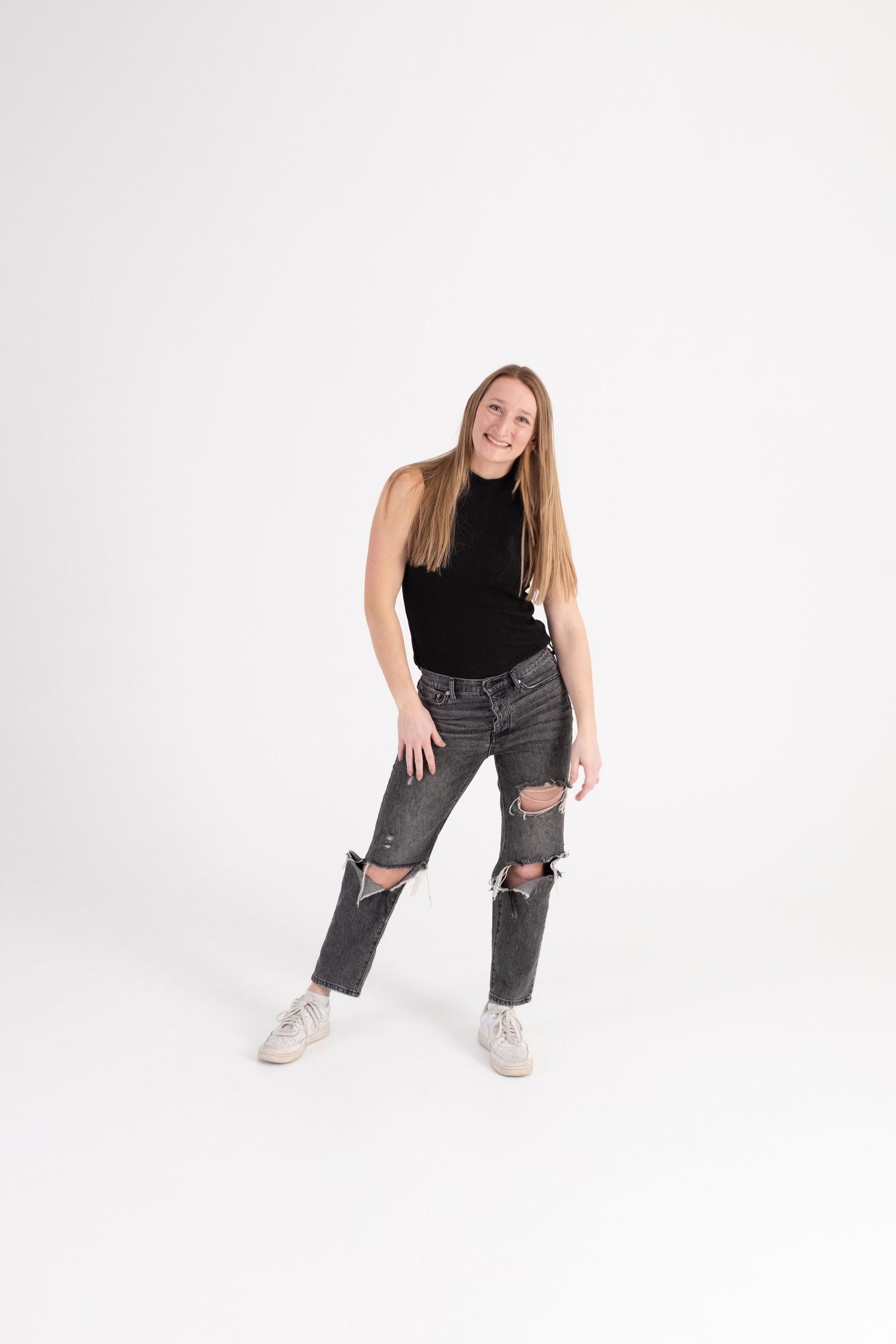 Hannah Lueck poses in a black sleeveless top, ripped black jeans and white sneakers against a white infinity wall.